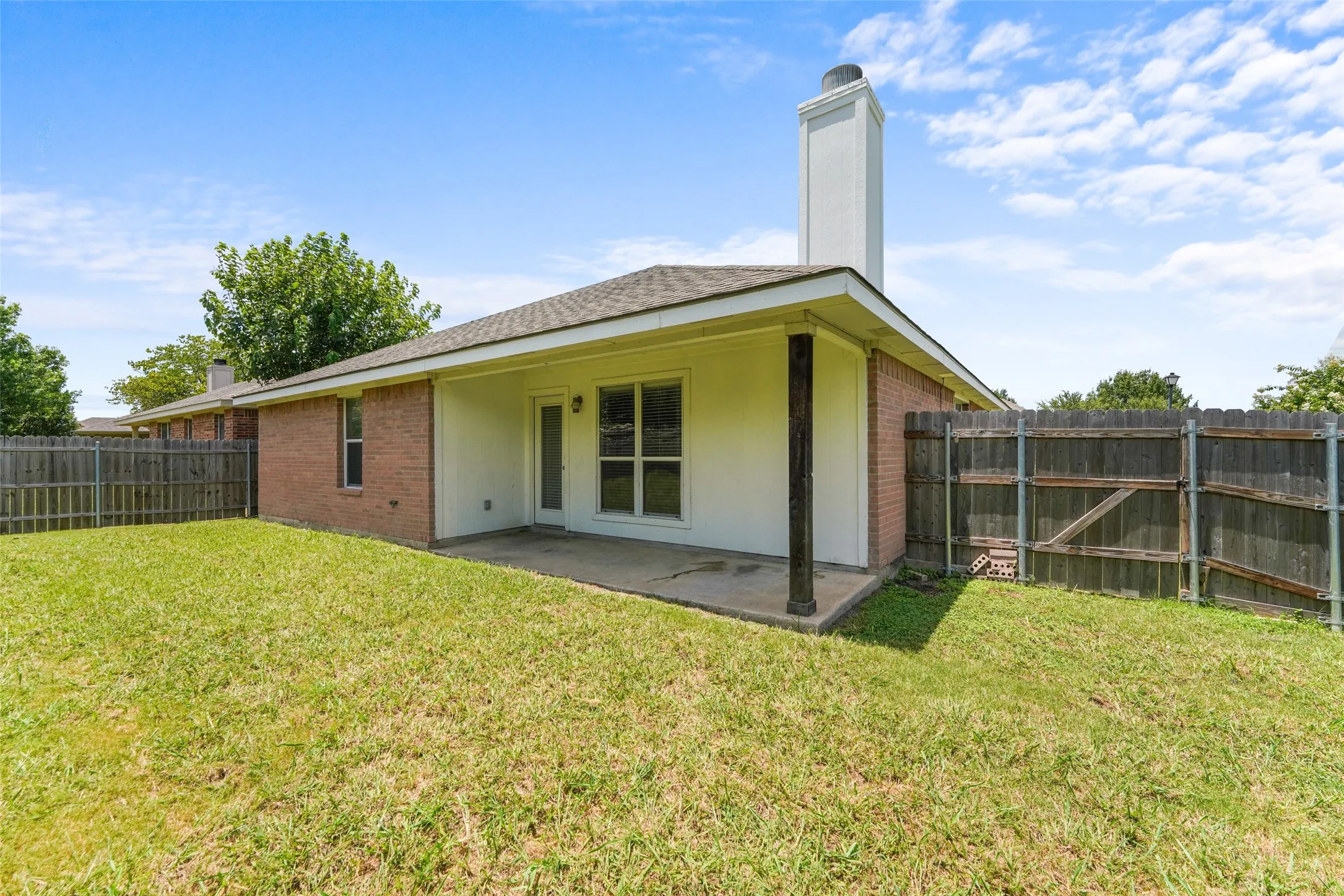 Spacious backyard featuring a covered patio, brick exterior, and a wood privacy fence