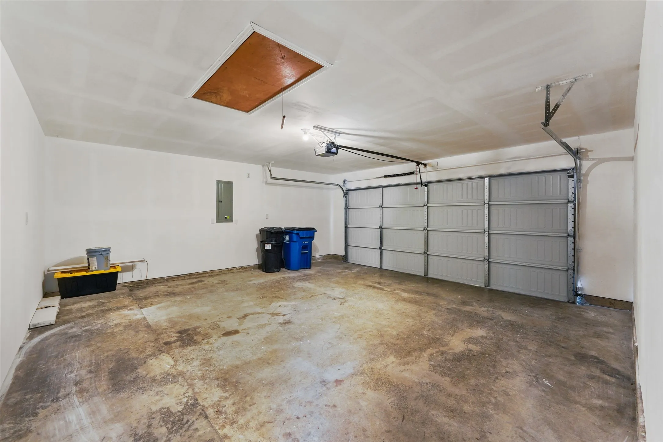 Spacious garage featuring a sectional garage door, exposed concrete flooring, white painted walls, and an attic access panel