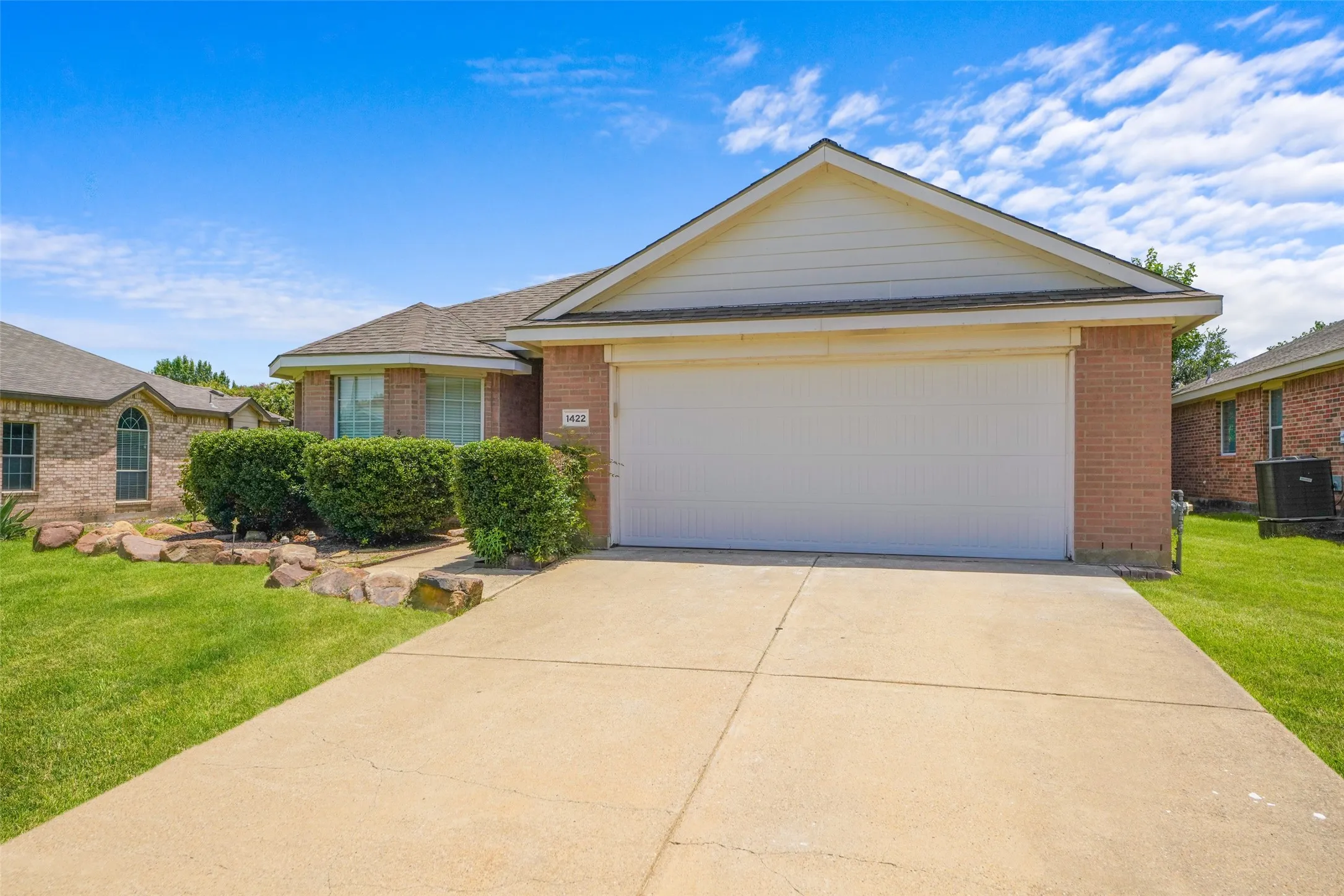 Brick exterior with a white garage door, concrete driveway, and front lawn