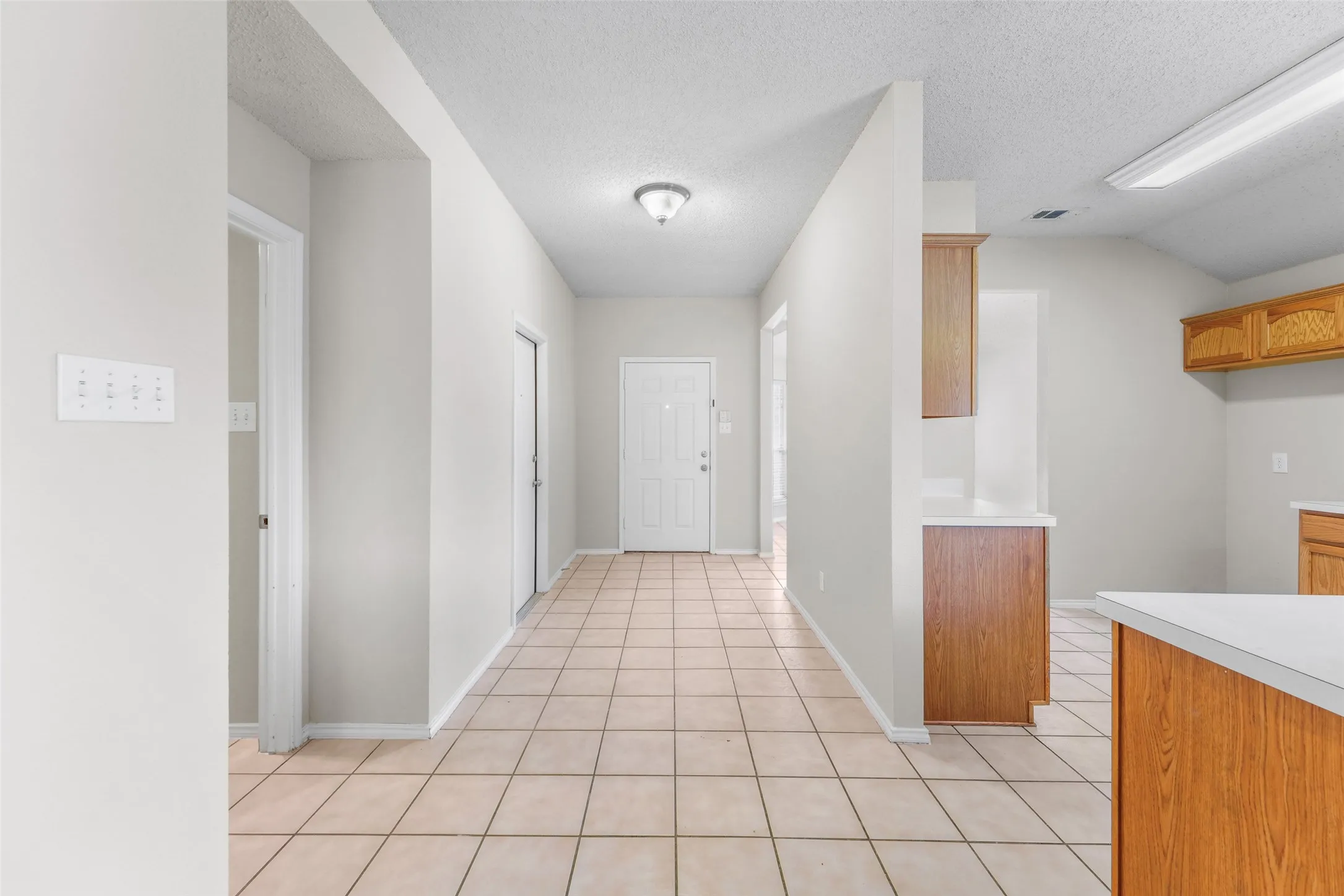 Tile flooring extending from the entry, a white paneled front door, and a kitchen area featuring wood-finish cabinetry and white countertops