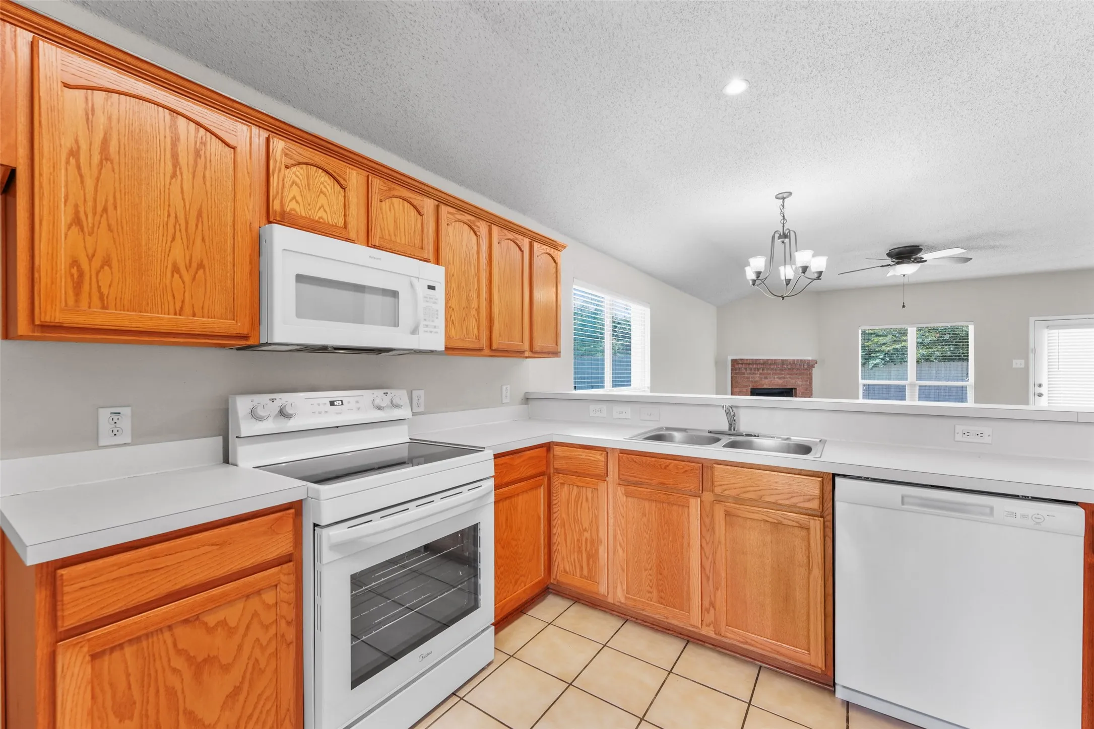 Kitchen featuring wood cabinetry, white countertops, and white appliances including a range, microwave, and dishwasher