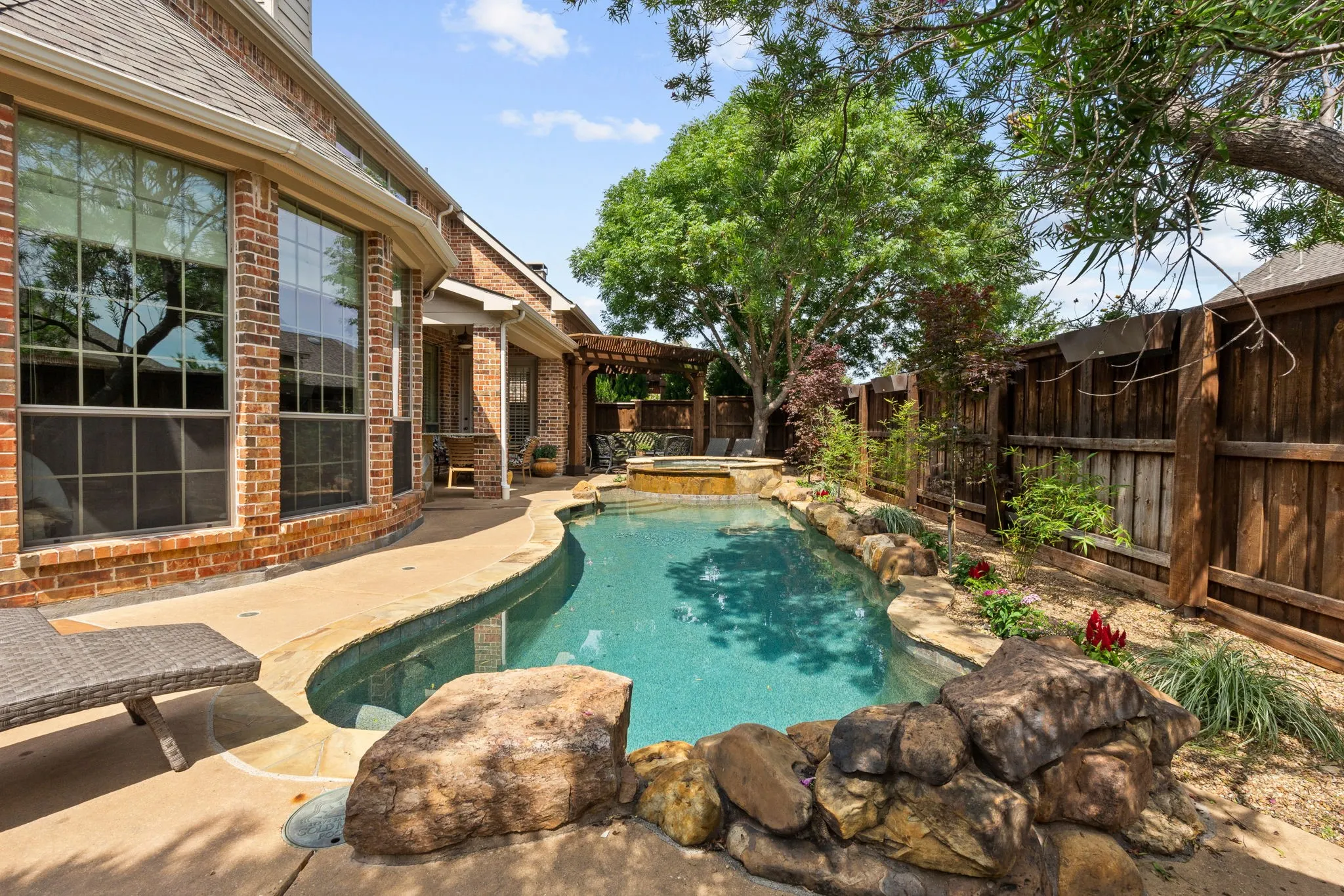 L-shaped swimming pool with an integrated spa, bordered by rock landscaping and a privacy fence