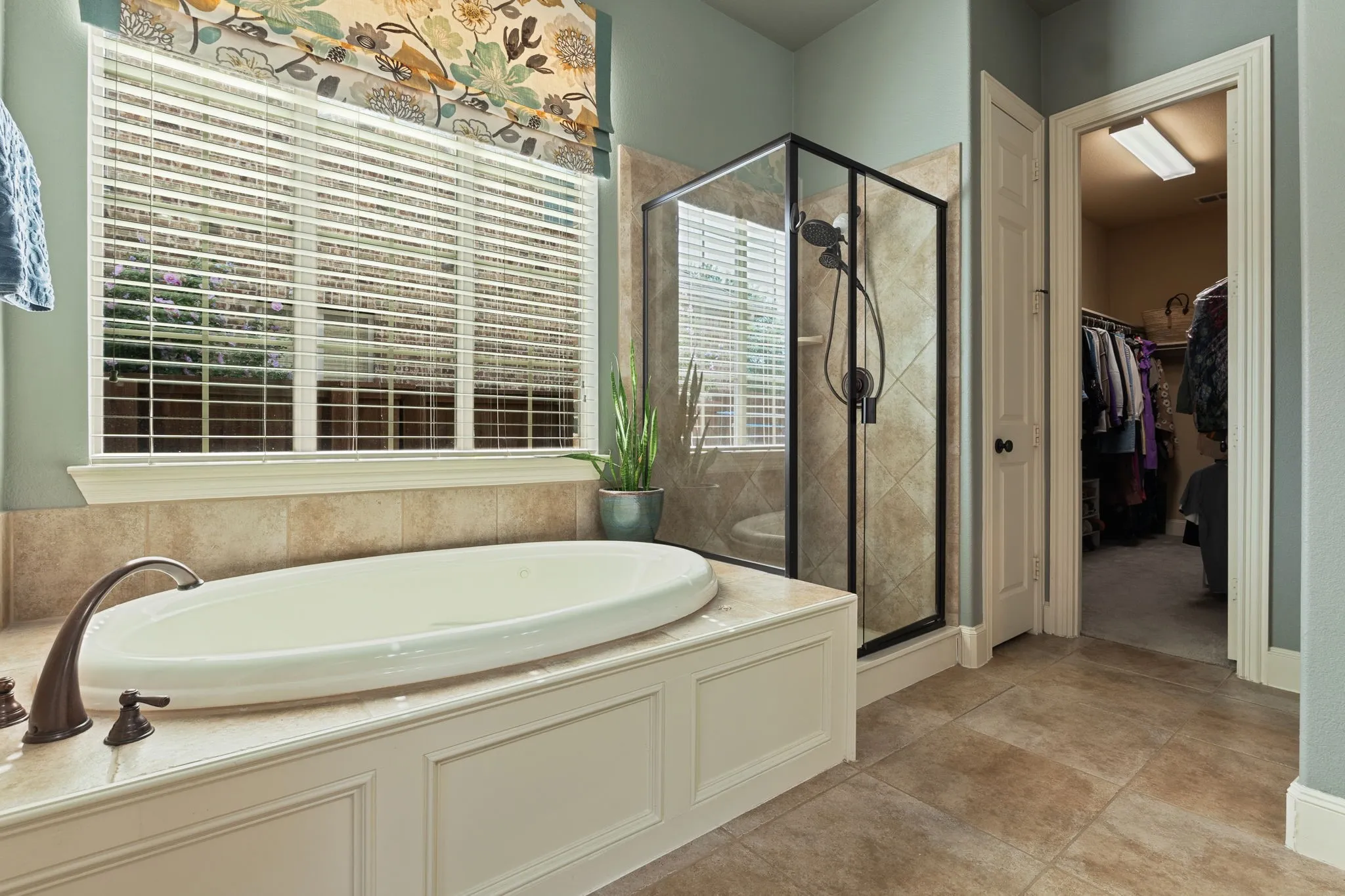 Built-in soaking tub with bronze-finish faucet, framed by a large window with white blinds and decorative valance