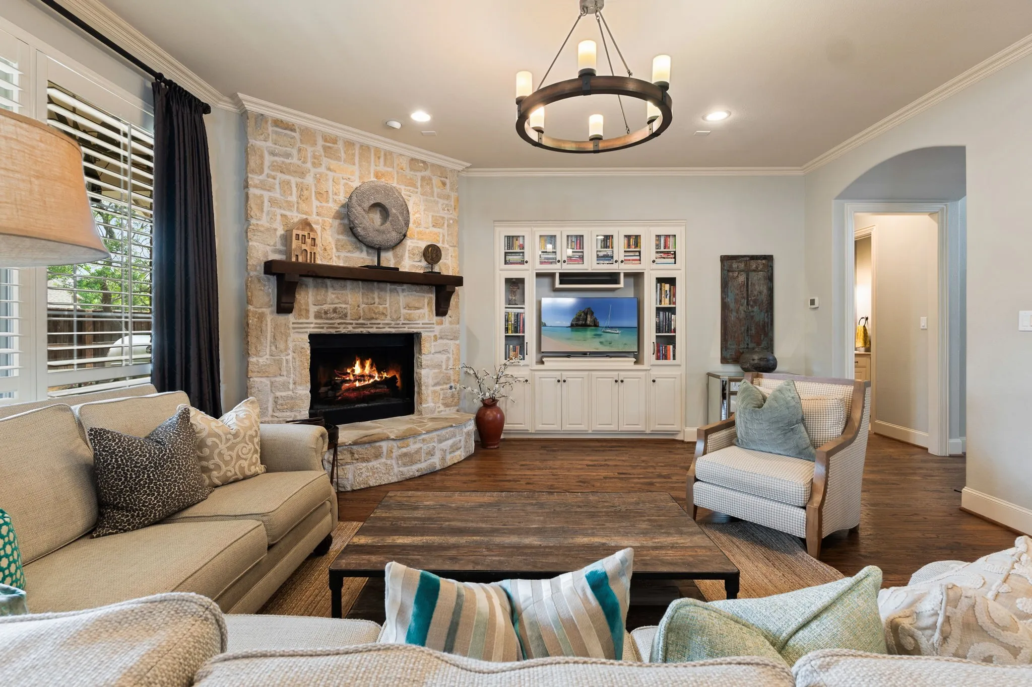 Living area featuring a stone-clad fireplace with a wood mantel, built-in media cabinetry with shelving, wood-finish flooring, and a circular chandelier