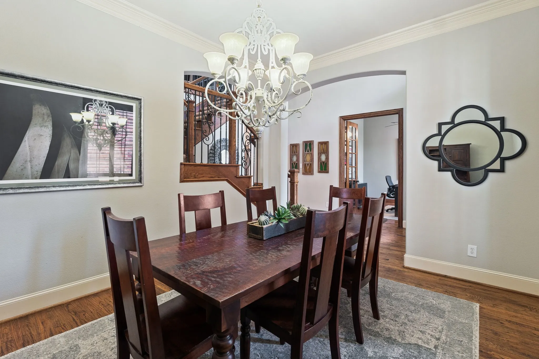 Hardwood flooring, crown molding, arched doorway, wrought iron staircase railing, and a decorative chandelier