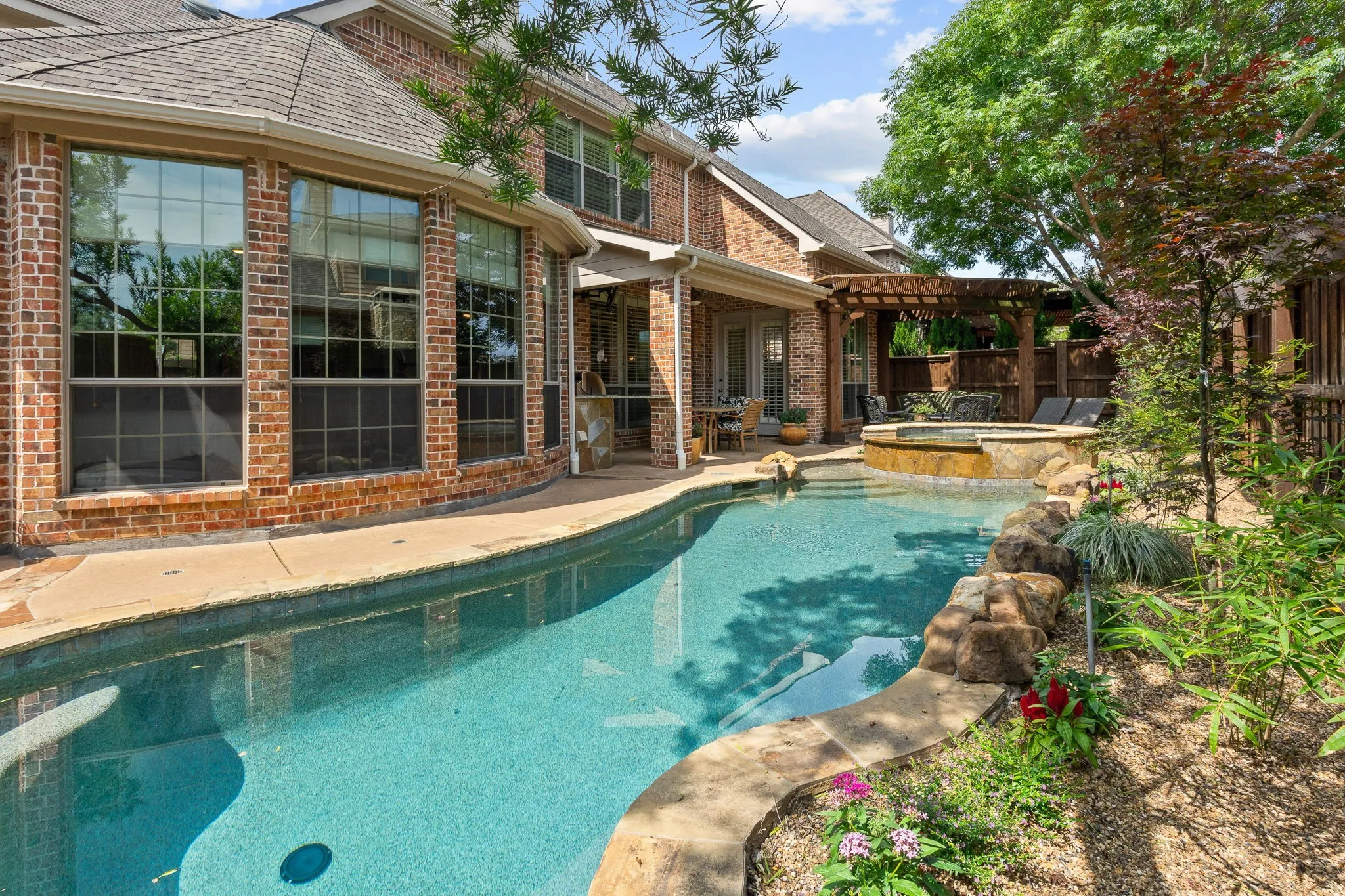 Brick exterior with multiple windows, inground pool with stone coping, separate spa, covered patio, and wood pergola