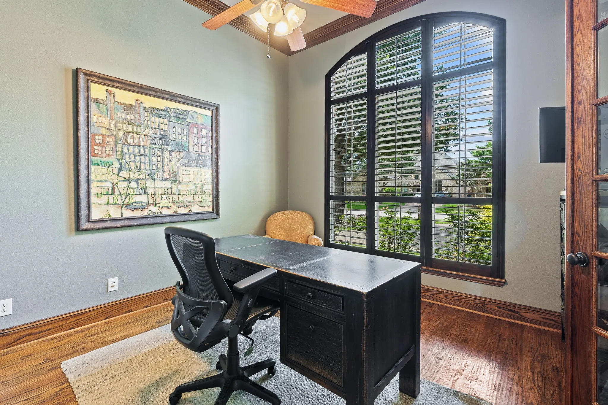 Arched window with plantation shutters, wood-finish flooring, ceiling fan, and crown molding