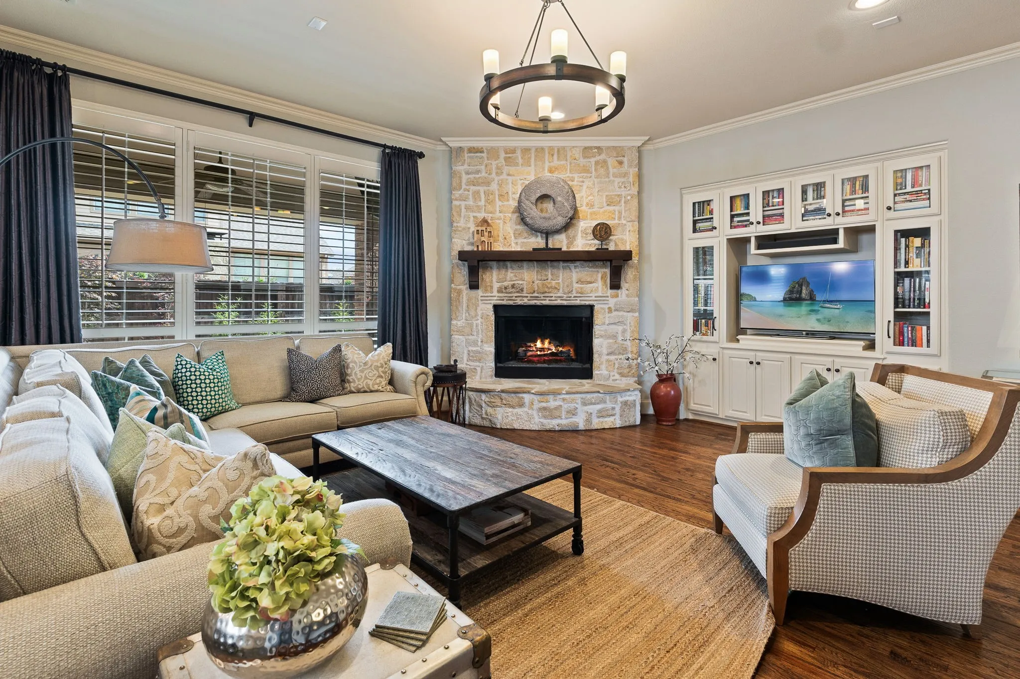 Corner stone-clad fireplace with a wood mantle, custom built-in entertainment center, plantation shutters, recessed lighting, and wood-finish flooring