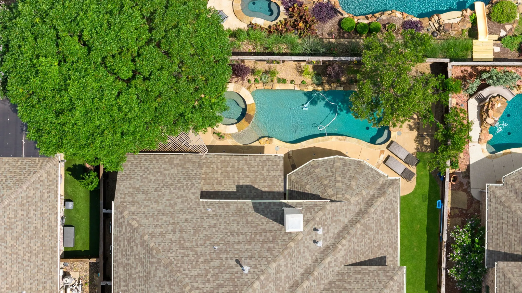 Curved swimming pool with an integrated spa, surrounded by a light-toned paved patio and mature trees