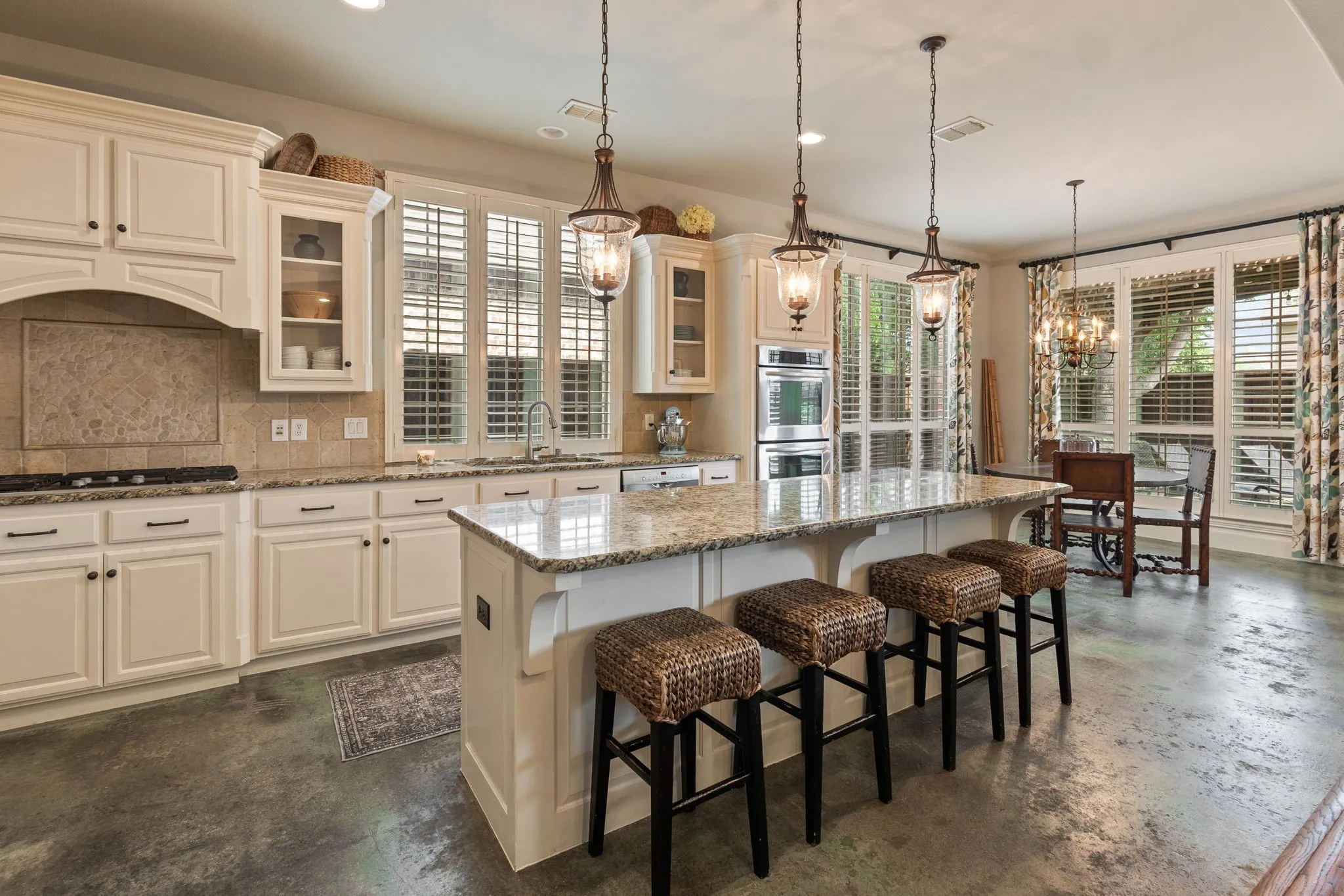 Open-concept kitchen featuring an oversized island with seating, cream cabinetry, stainless steel double ovens, and a gas cooktop