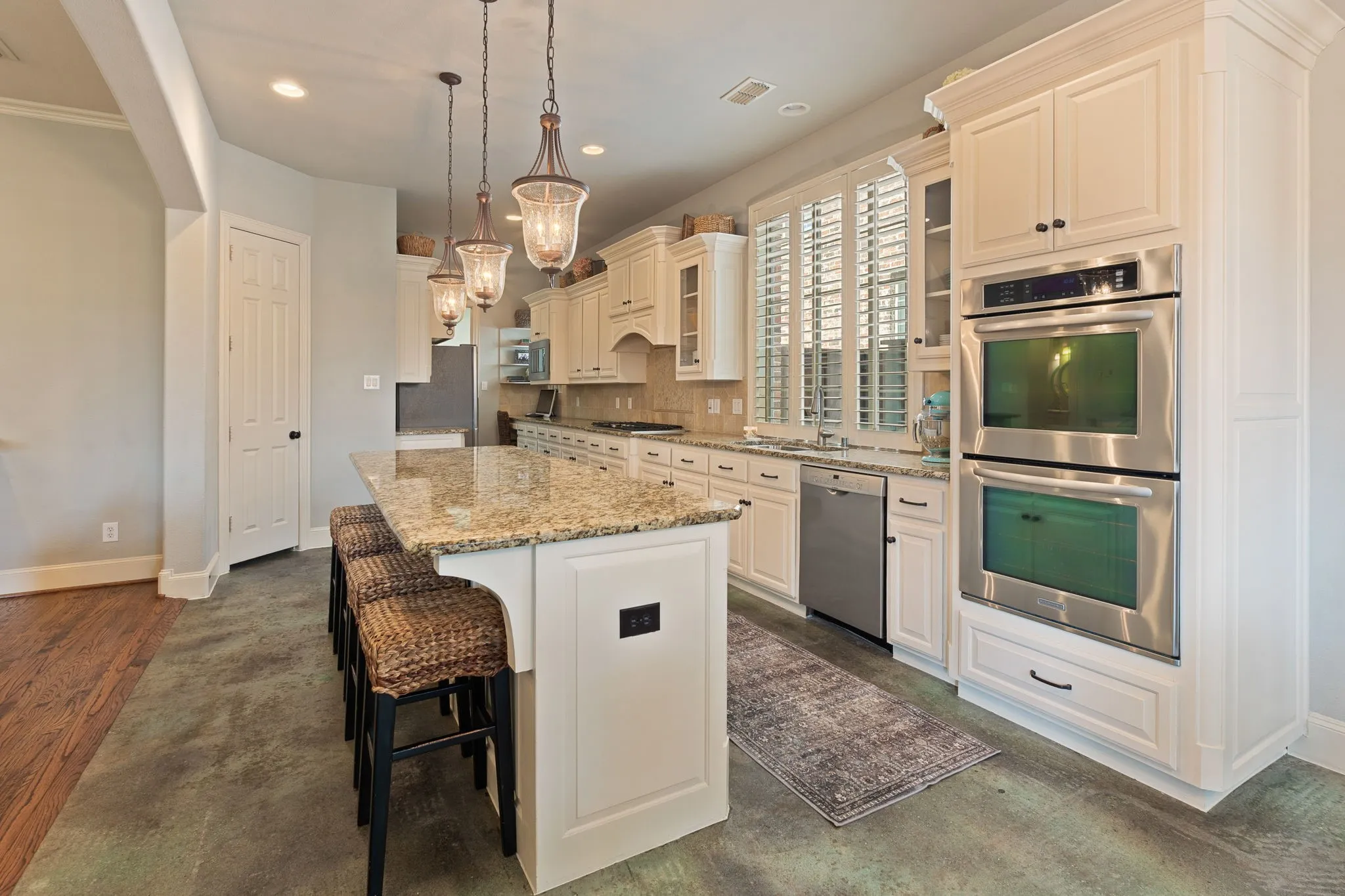 Kitchen featuring a granite-topped island with pendant lighting, white cabinetry, stainless steel double ovens, and a stainless steel dishwasher
