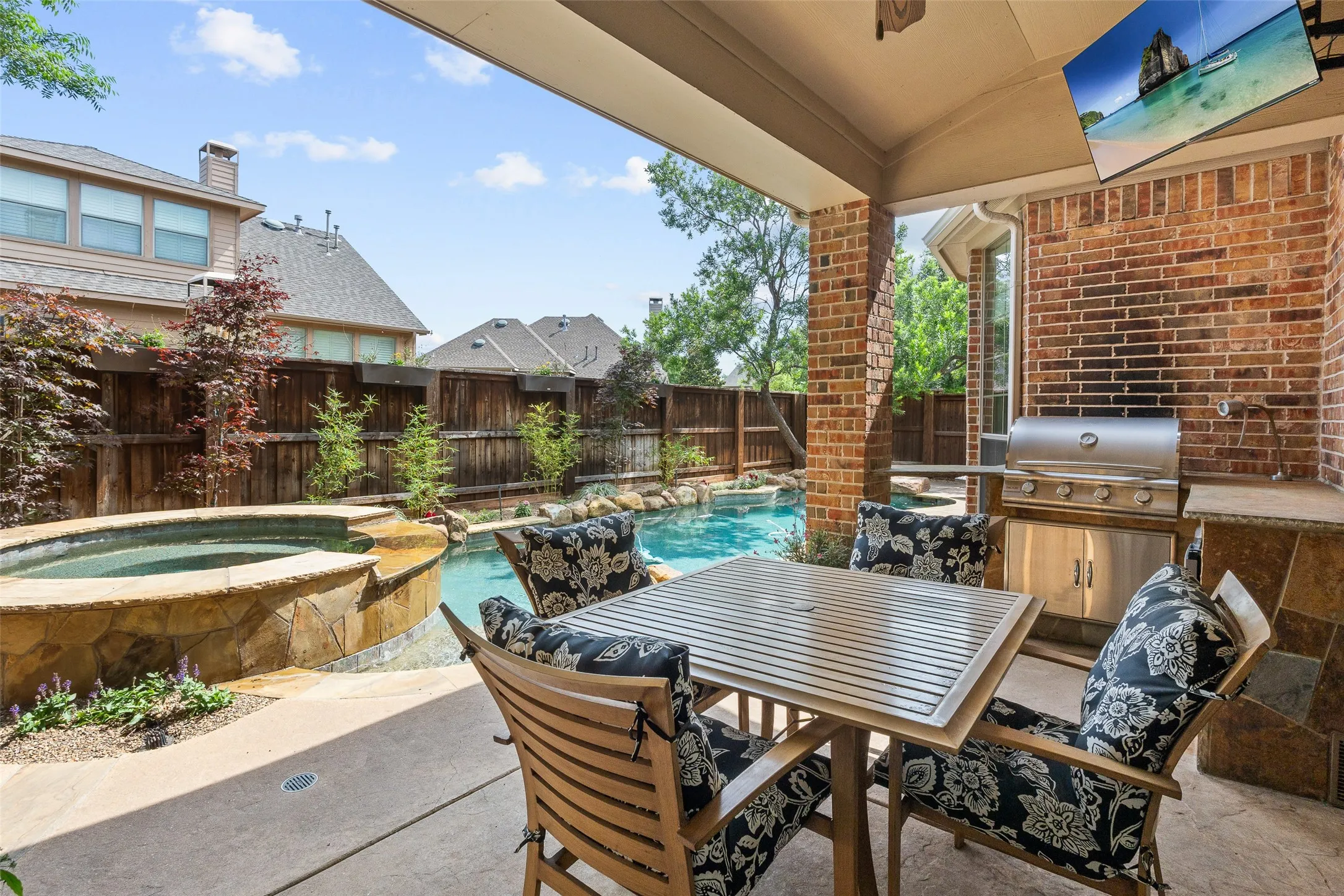 Covered patio with integrated outdoor kitchen, built-in stainless steel grill, stone-accented hot tub, and swimming pool