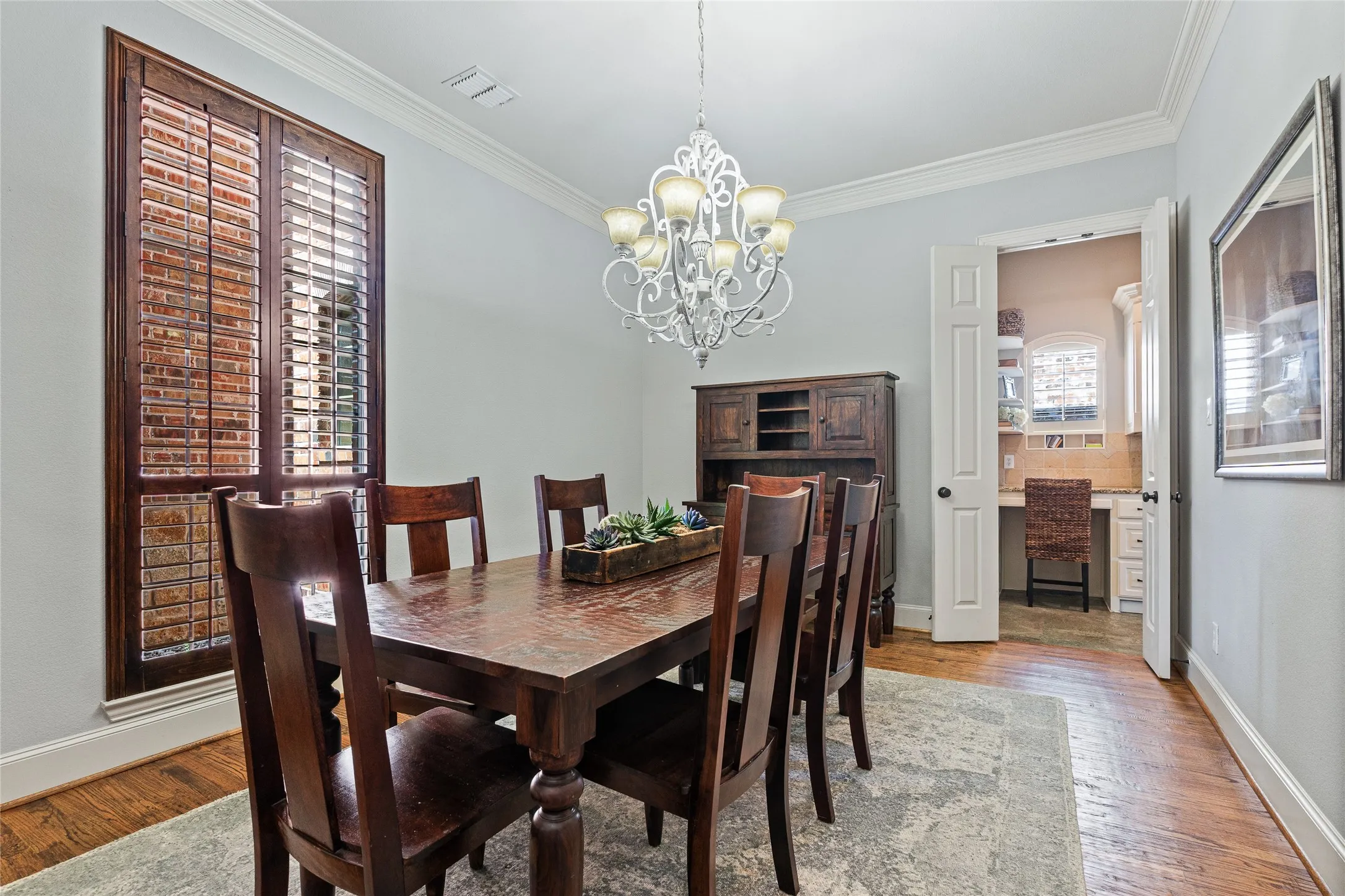 Hardwood flooring, crown molding, and a chandelier illuminate this dining space