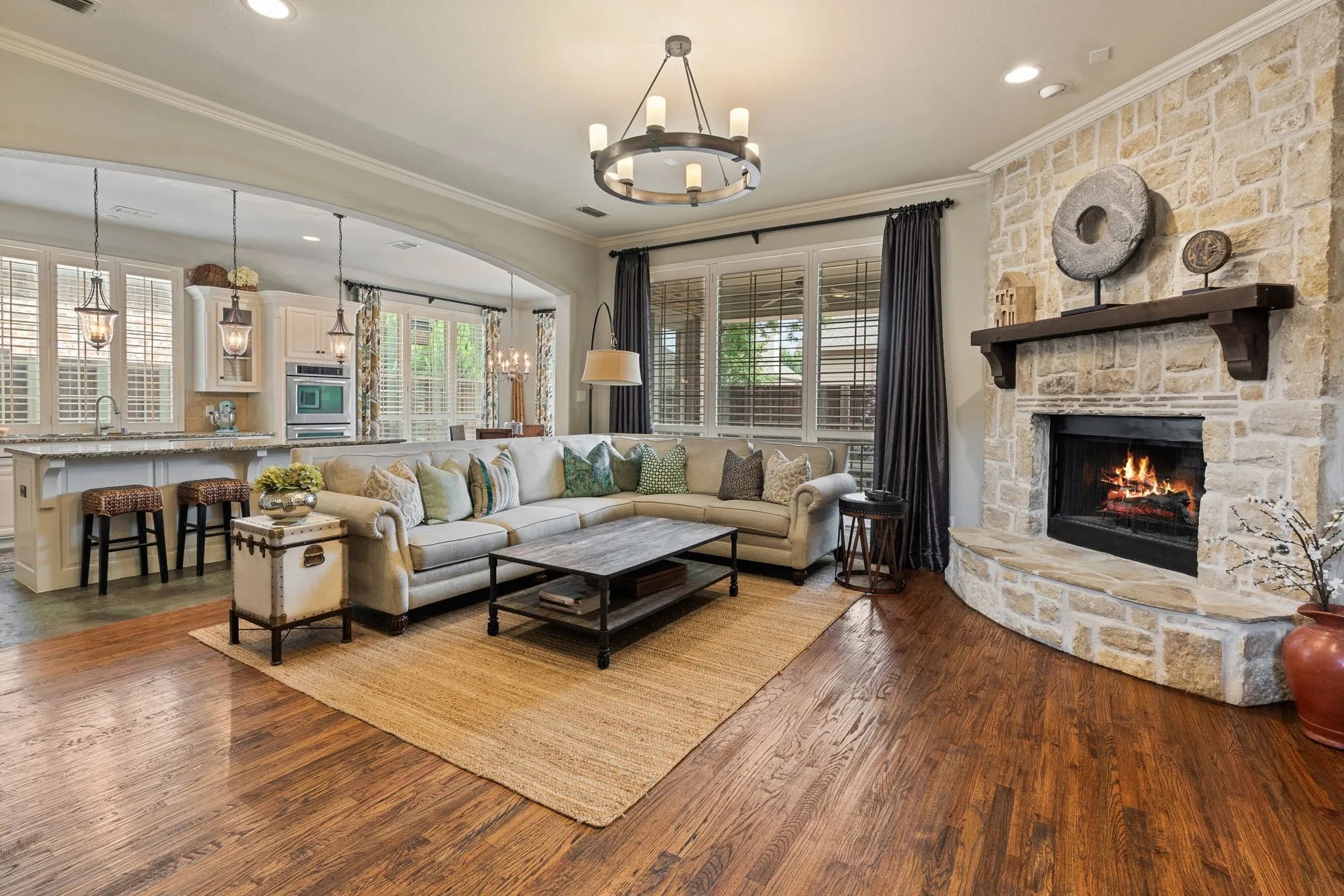 Spacious living area featuring rich wood-finish flooring, a stone-clad fireplace with a substantial mantel, and a multi-light chandelier