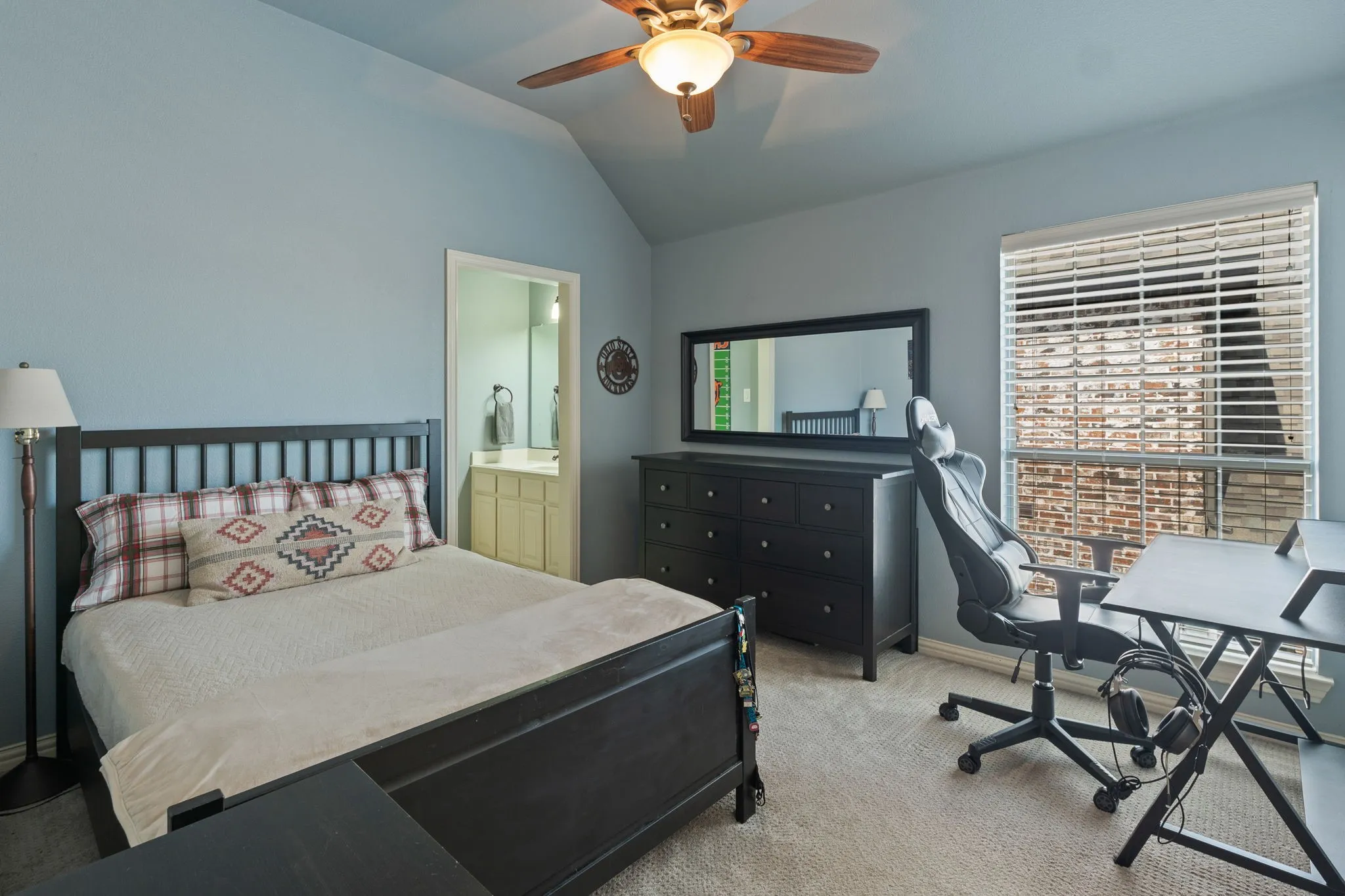 Vaulted ceiling bedroom with soft blue wall color, featuring a ceiling fan with integrated lighting, a window with horizontal blinds, and carpeted flooring