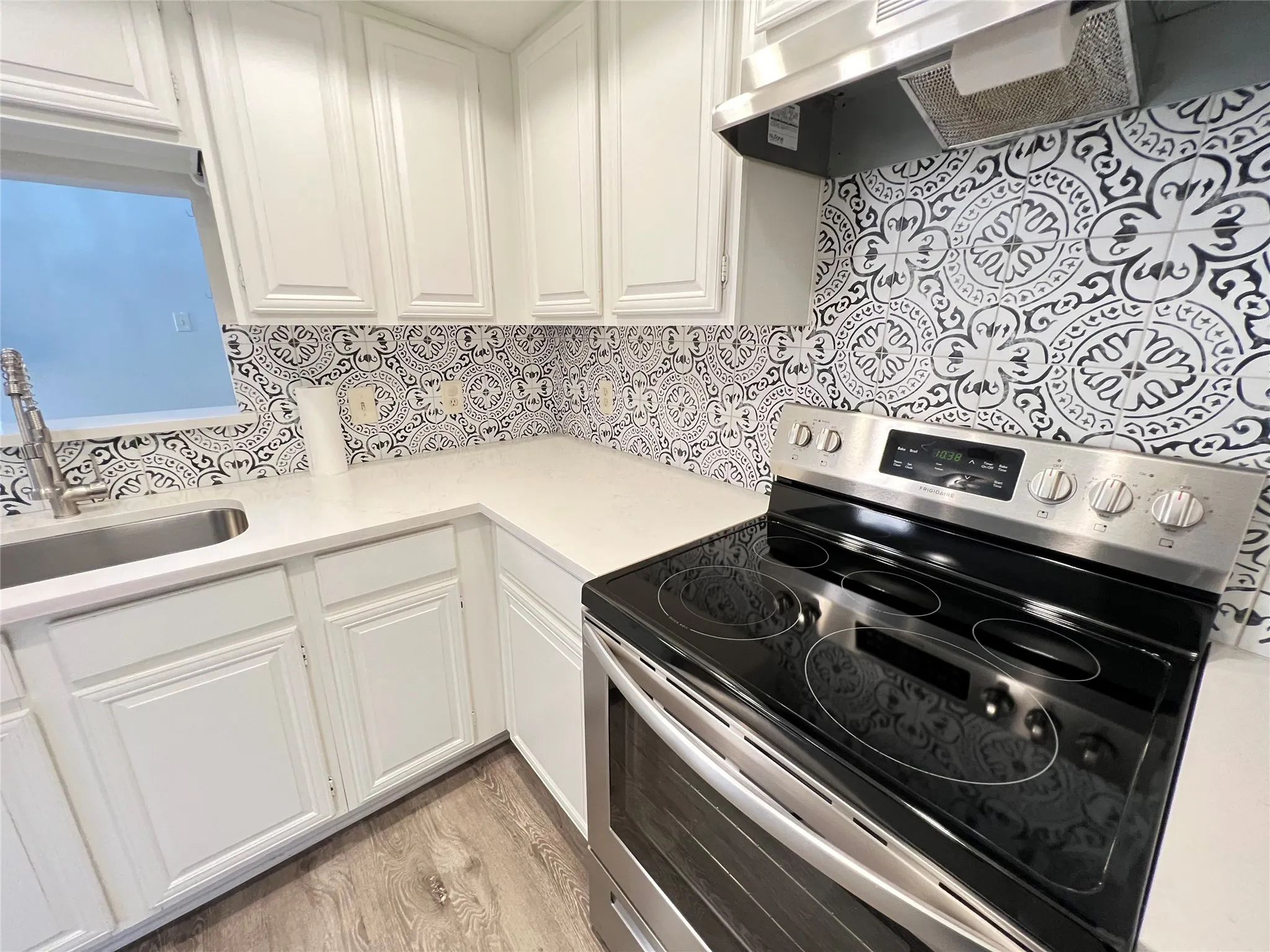 Kitchen featuring white cabinetry, quartz countertops, a patterned tile backsplash, stainless steel appliances, and wood-finish flooring