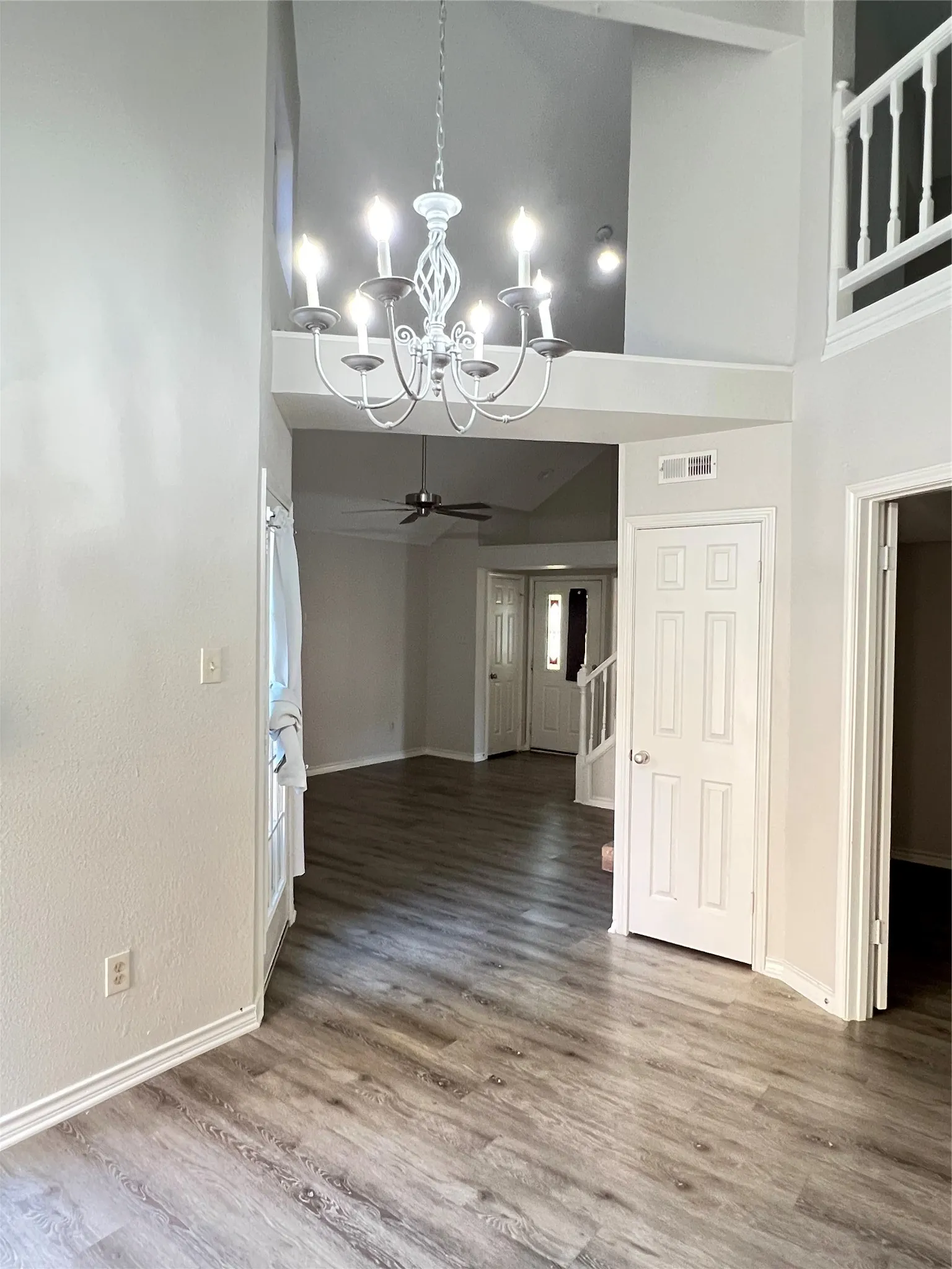 Vaulted ceilings featuring a chandelier, wood-finish flooring, white trim, and a white six-panel door