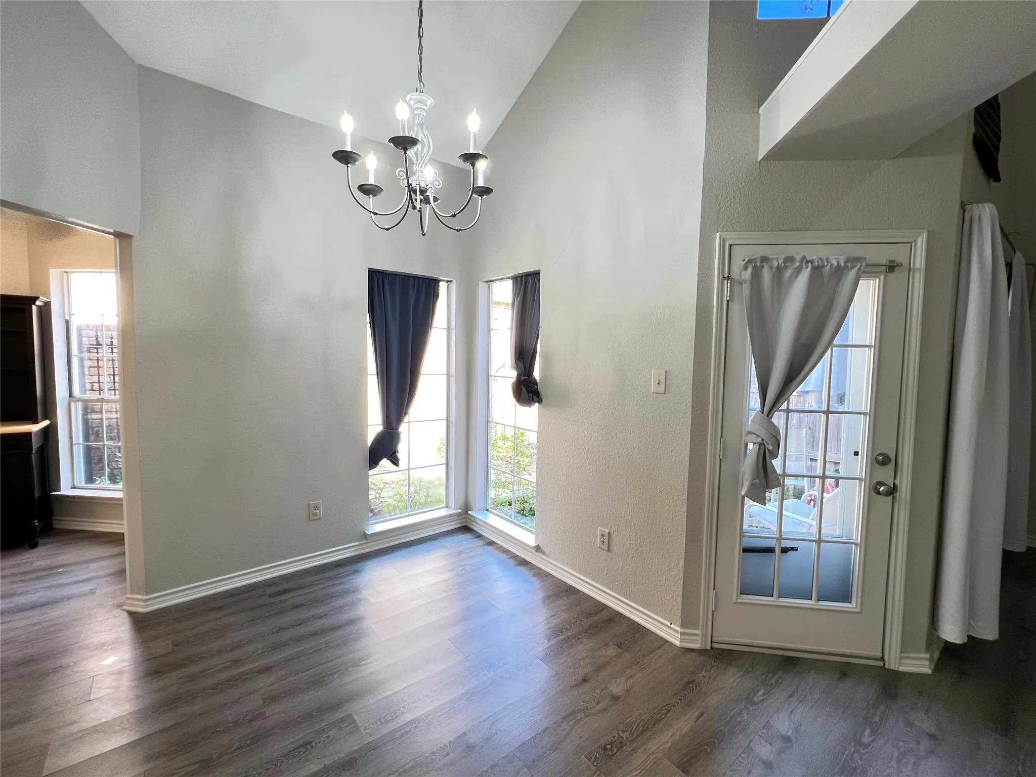 Vaulted ceiling room featuring wood-finish flooring, a glass-paned door, and multiple windows