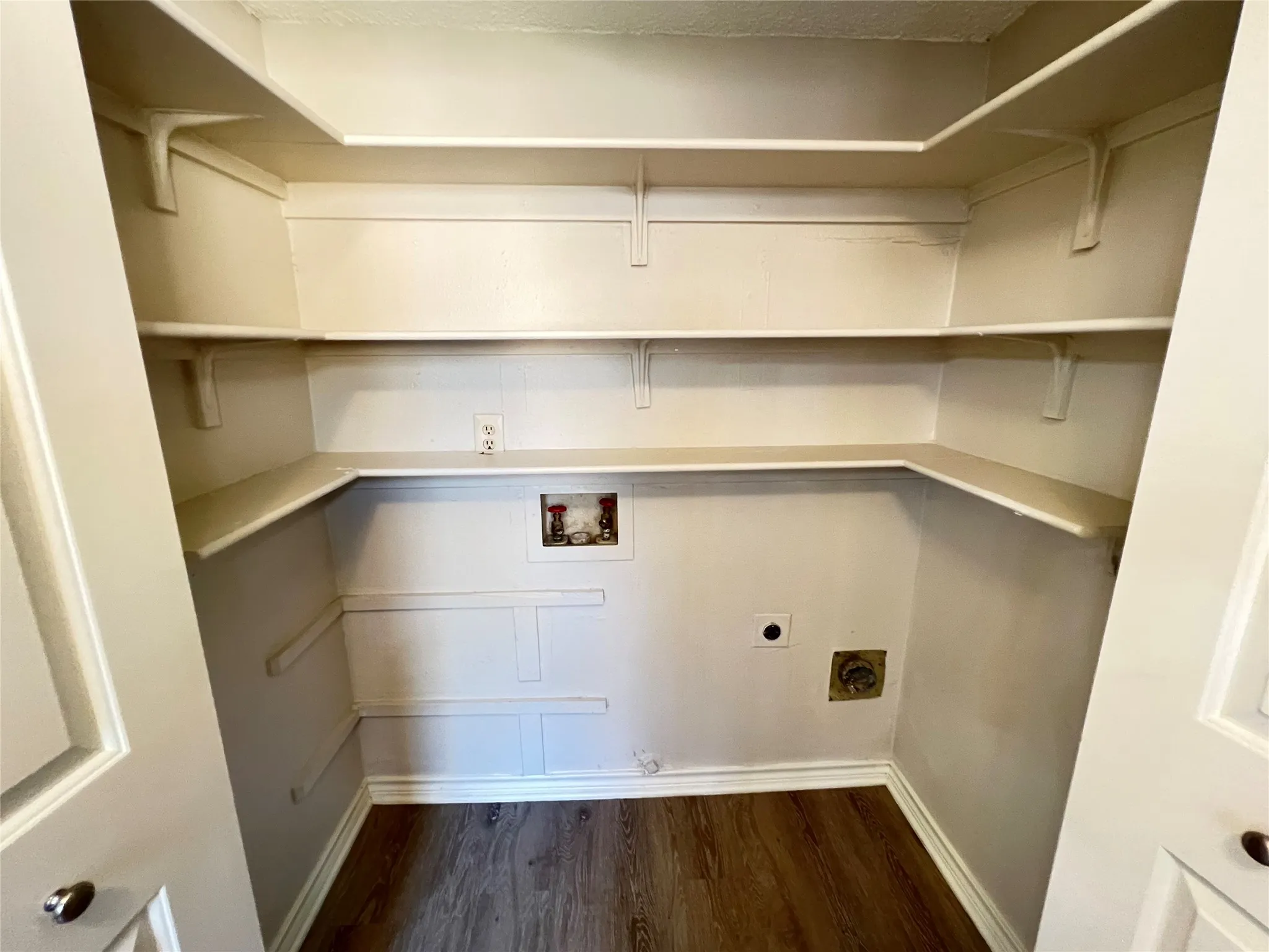 Dedicated laundry area with hookups, integrated shelving, and wood-finish flooring