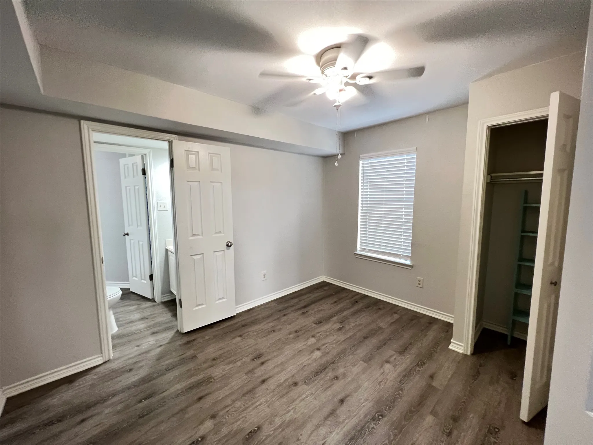 Spacious room featuring wood-finish flooring, neutral wall tones, a ceiling fan, and a window with blinds