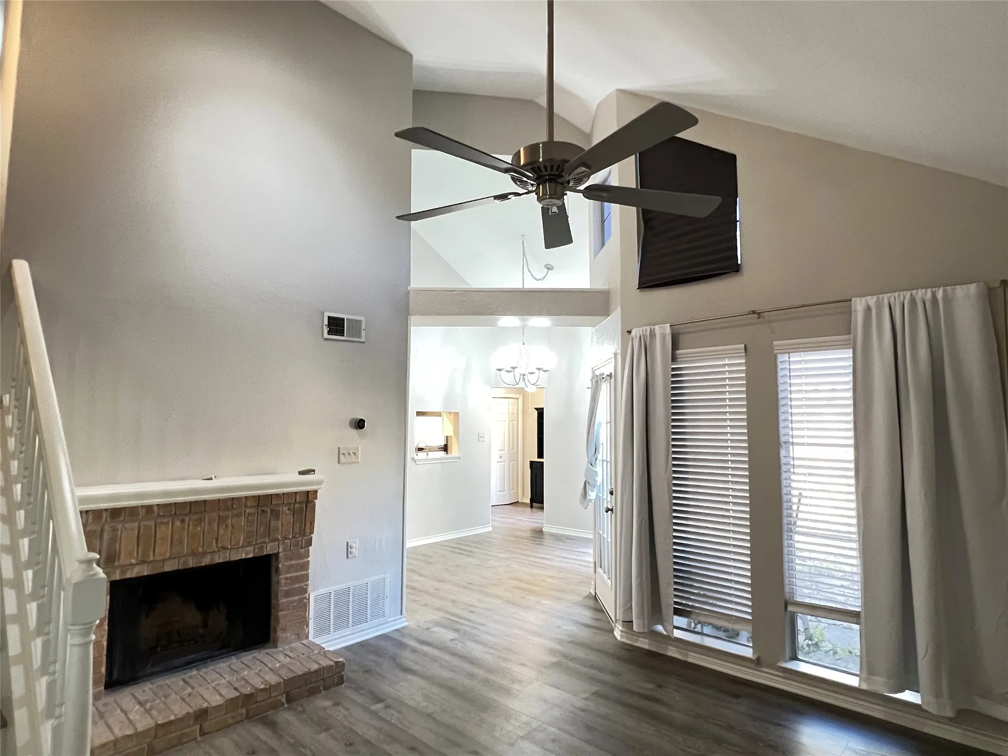 Living area featuring vaulted ceilings, a brick fireplace with a white mantel, and wood-finish flooring