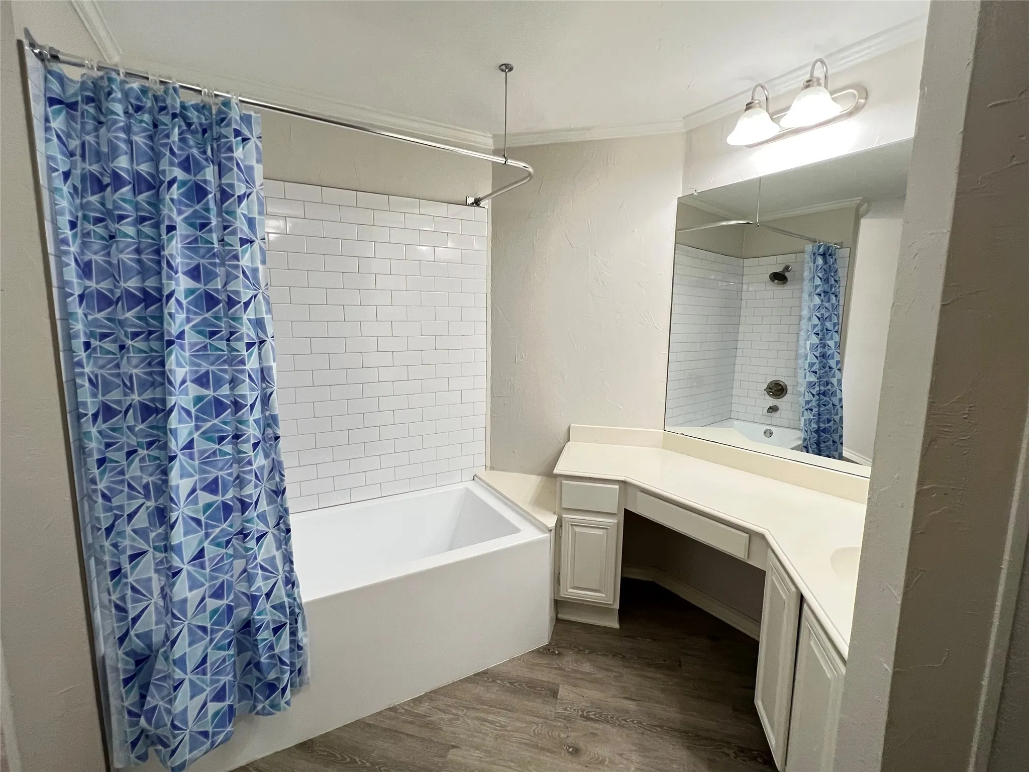 Bathroom featuring a white subway tile tub surround, built-in vanity with solid surface countertop, integrated sink, and wood-finish flooring
