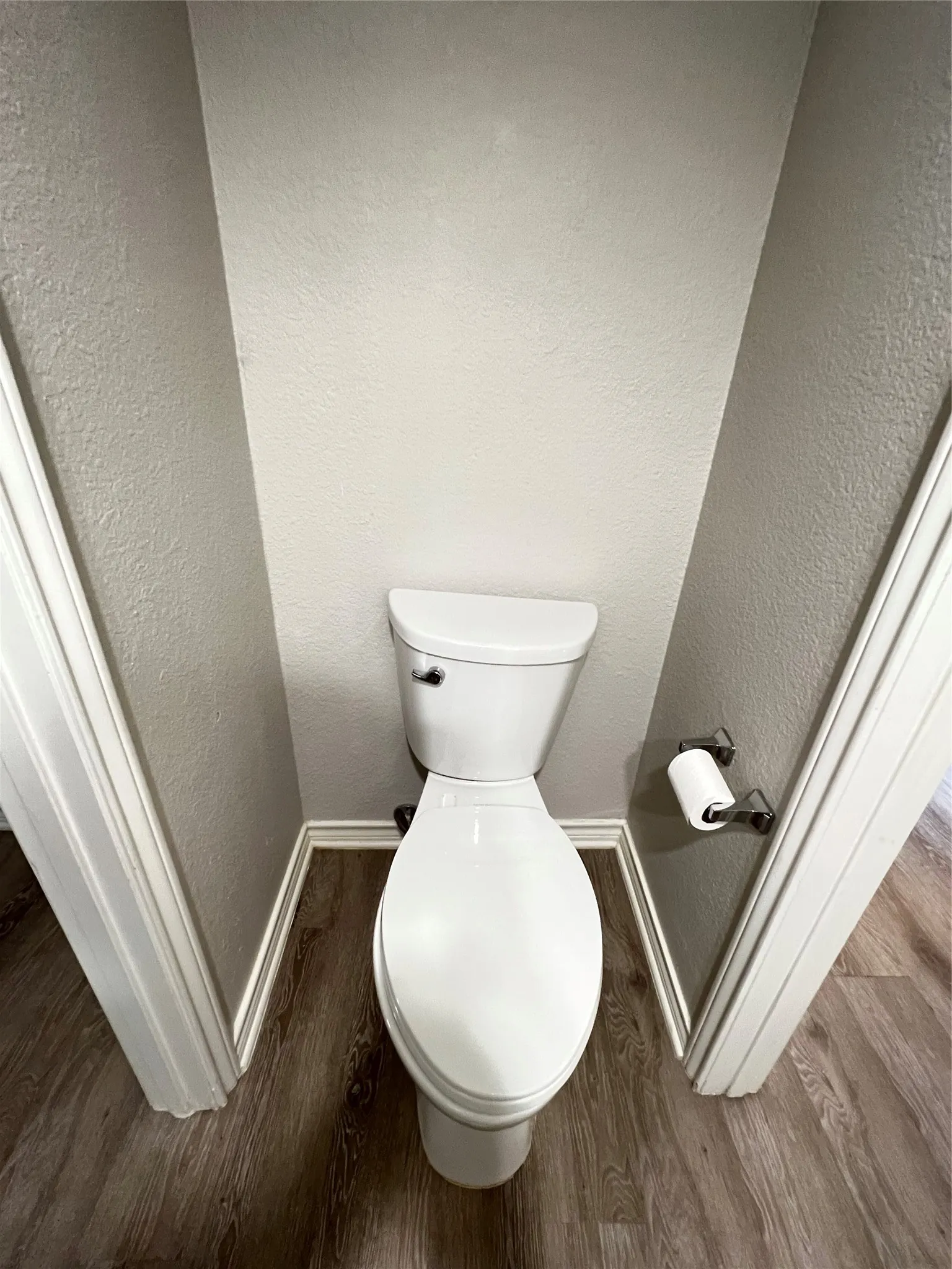 Water closet featuring a white commode, wood-finish flooring, and a wall-mounted toilet paper holder