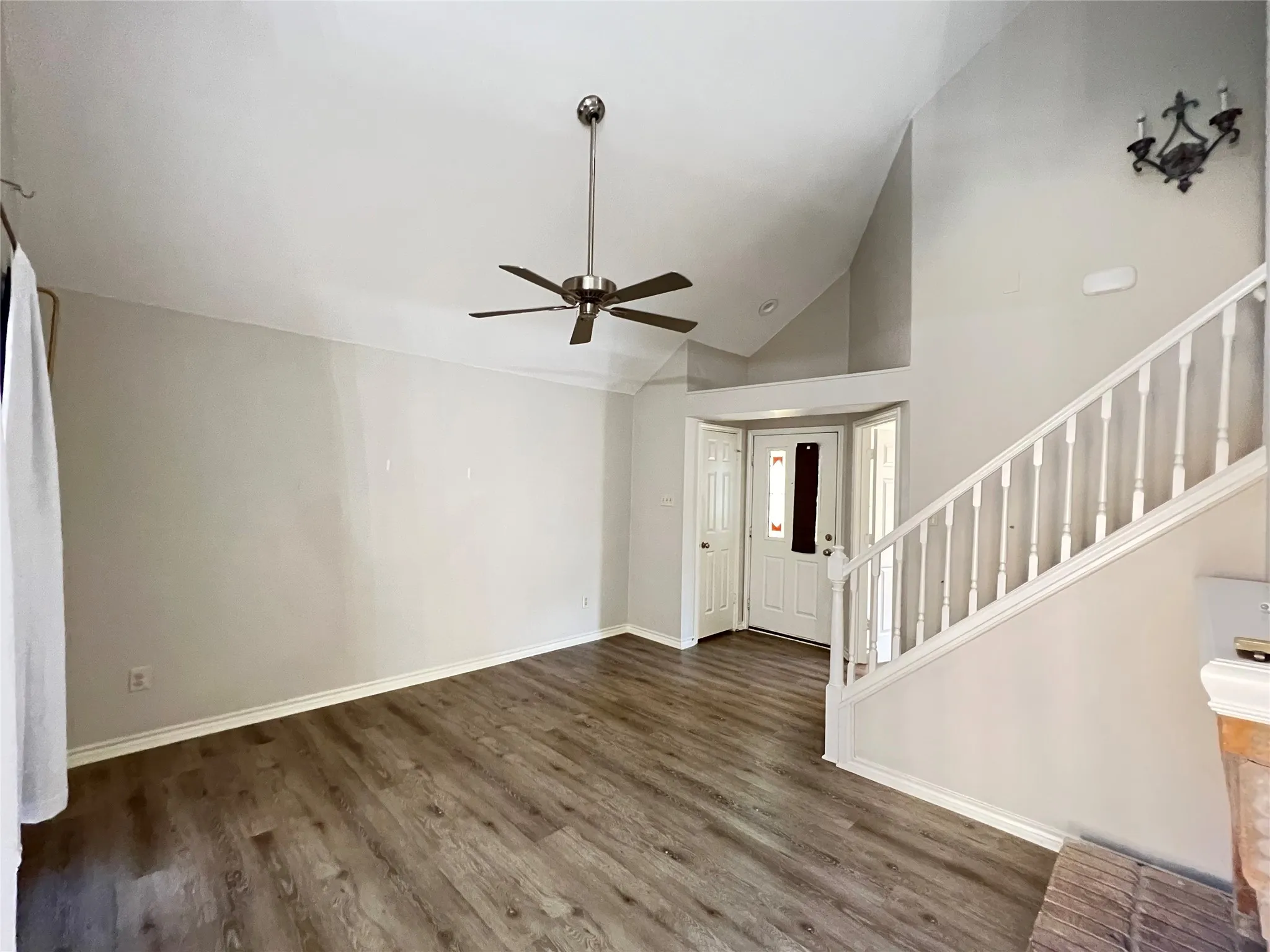 Vaulted ceiling living space featuring wood-finish flooring, a ceiling fan, and a light-filled entryway with a decorative front door