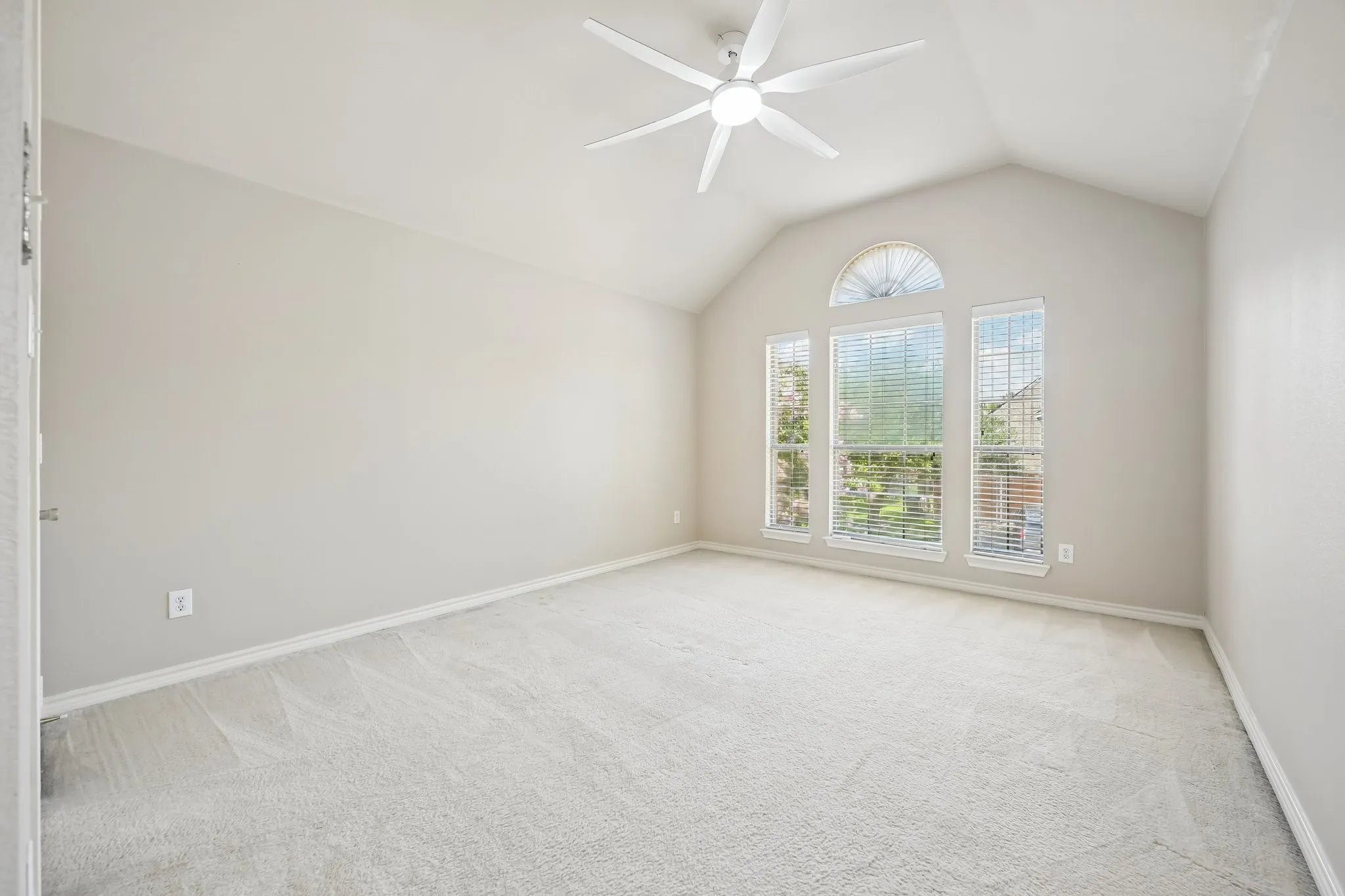 Room featuring vaulted ceilings, a contemporary ceiling fan, and large windows with arched transom