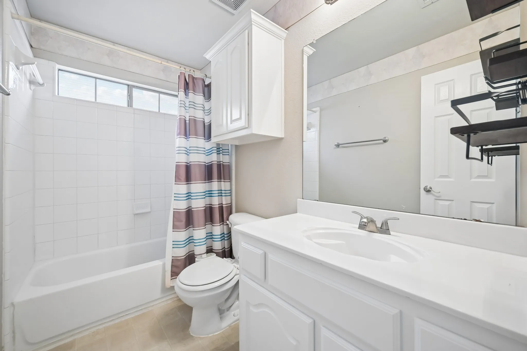 Bathroom featuring a white vanity with an integrated sink and chrome faucet, an overhead white cabinet, a full-width mirror, and a white tile shower-tub combination with an upper window