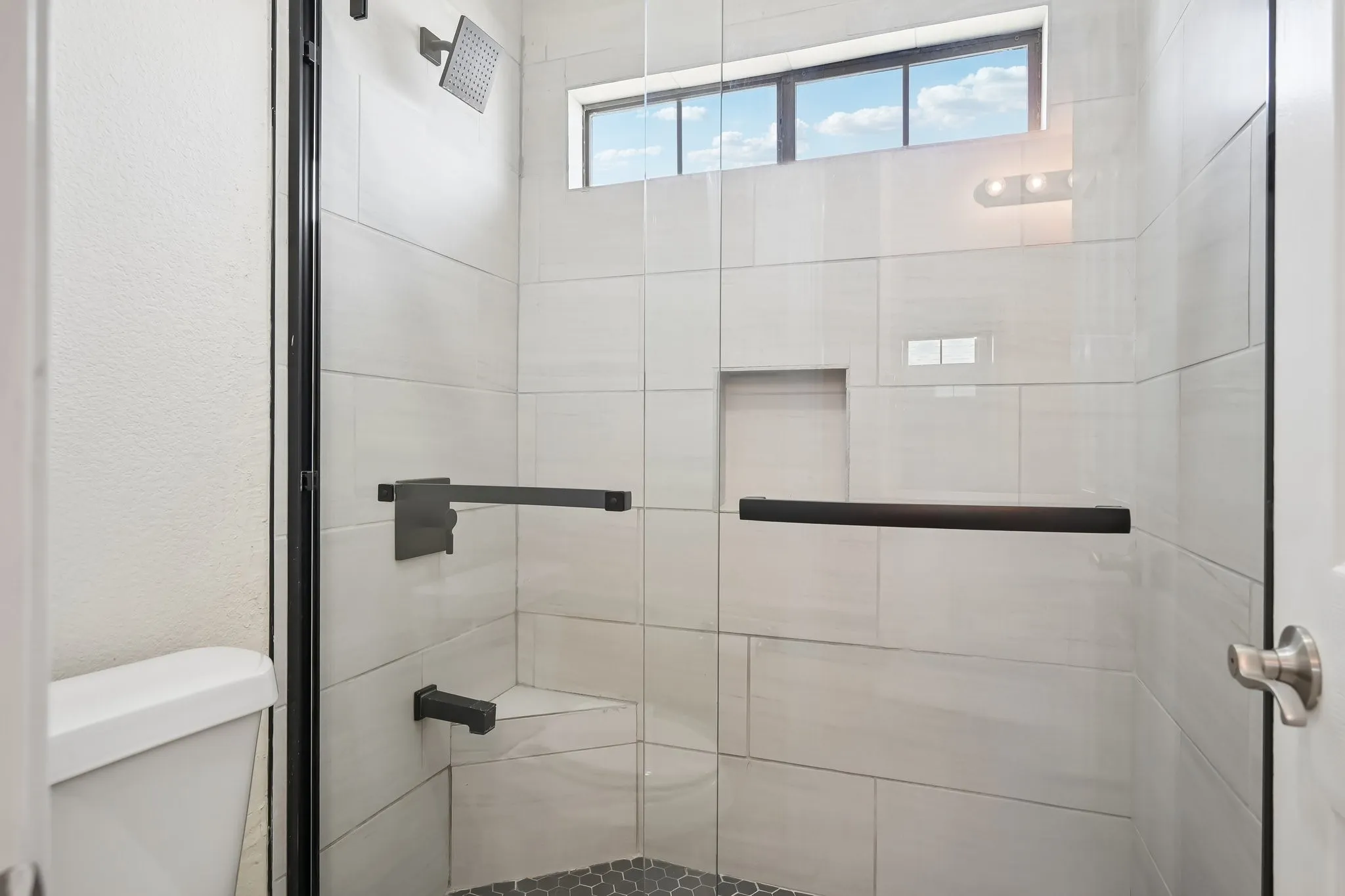 Walk-in shower featuring a frameless glass enclosure with matte black hardware, white rectangular tile surrounds, a built-in bench, a recessed niche, and a hexagonal mosaic tile floor