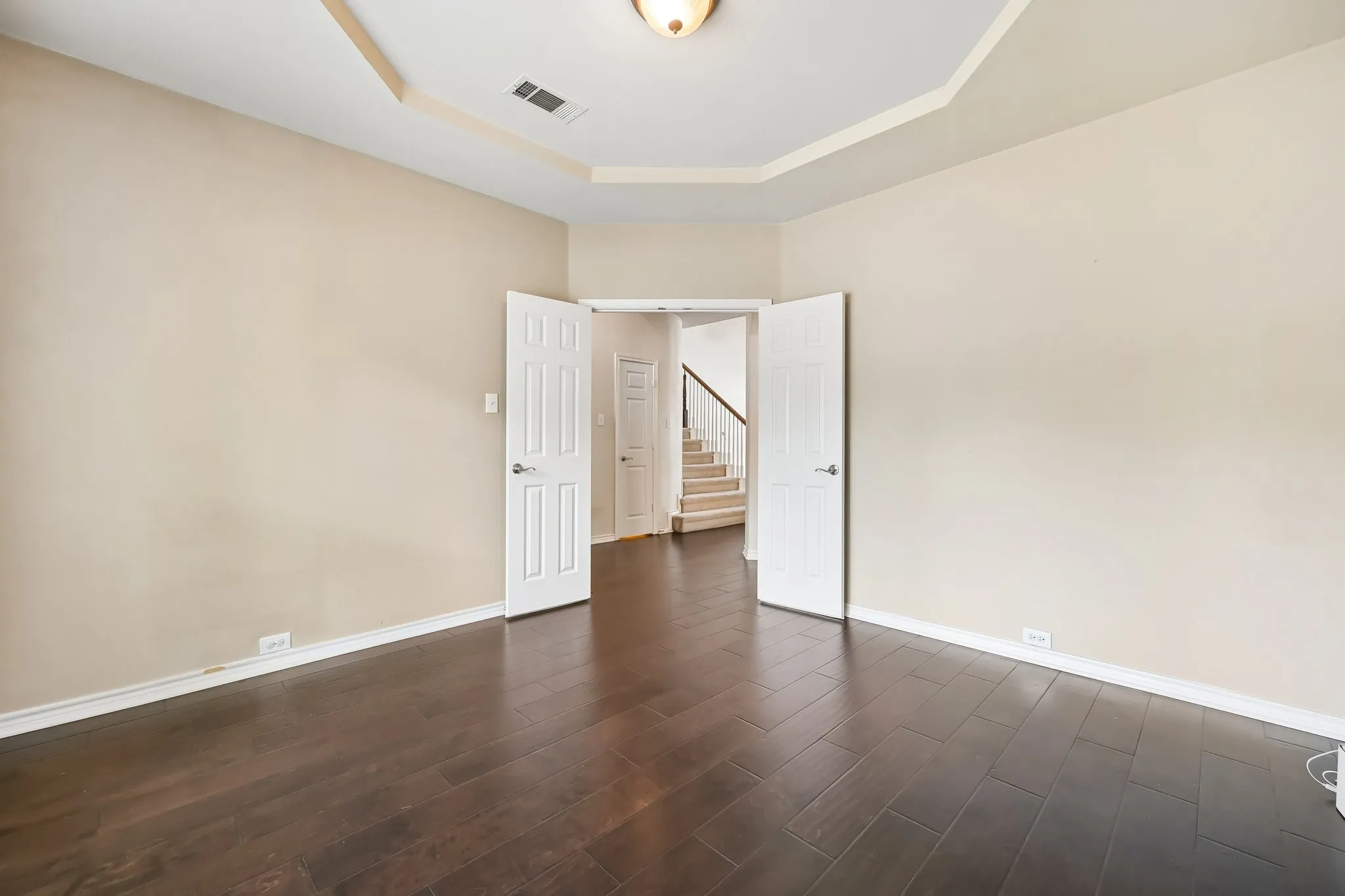 Spacious room featuring wood-finish flooring, neutral-toned walls, and a recessed ceiling with a central light fixture
