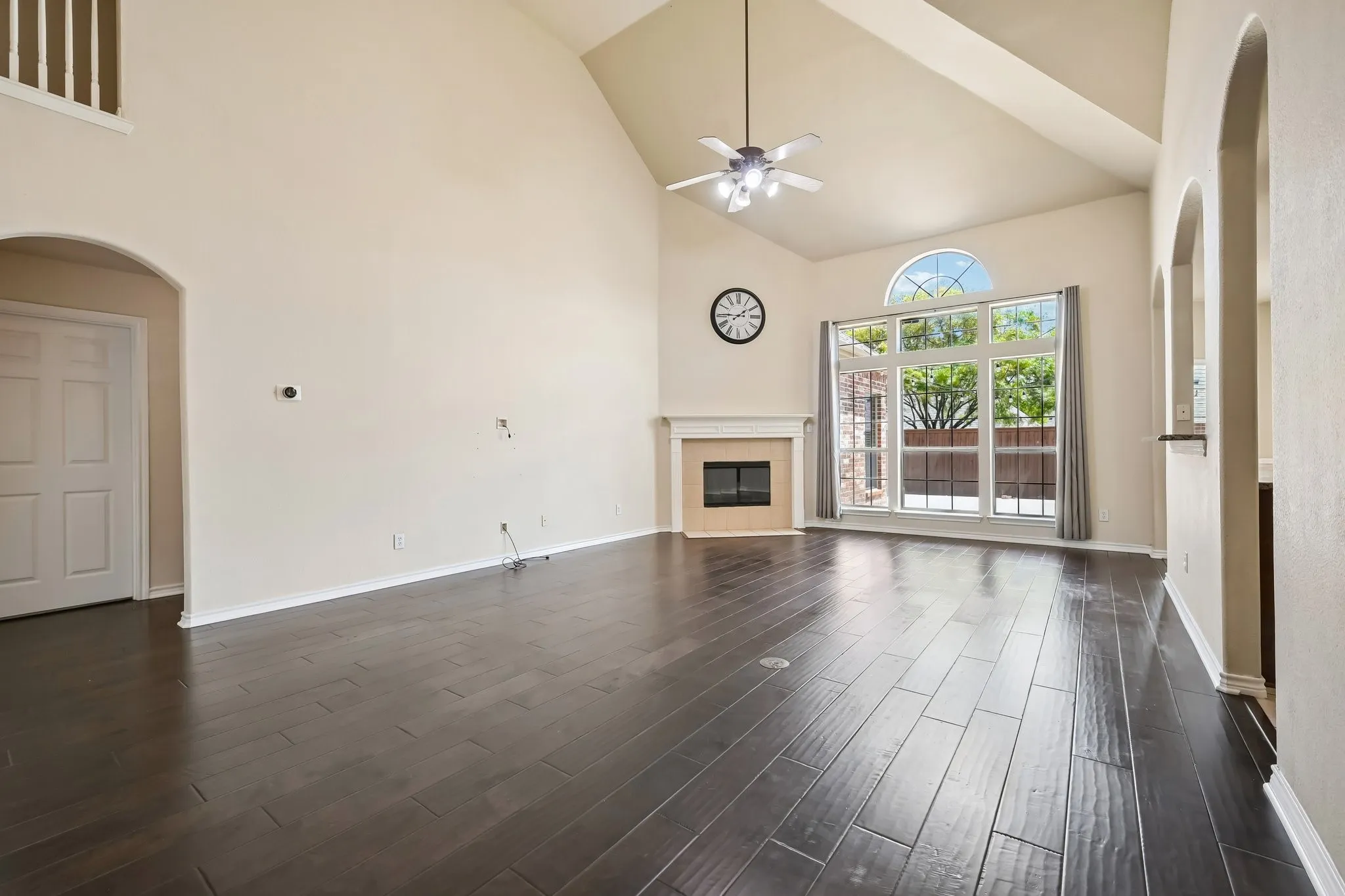 Spacious room featuring soaring vaulted ceilings, dark wood-finish flooring, and a fireplace with a light-toned mantle