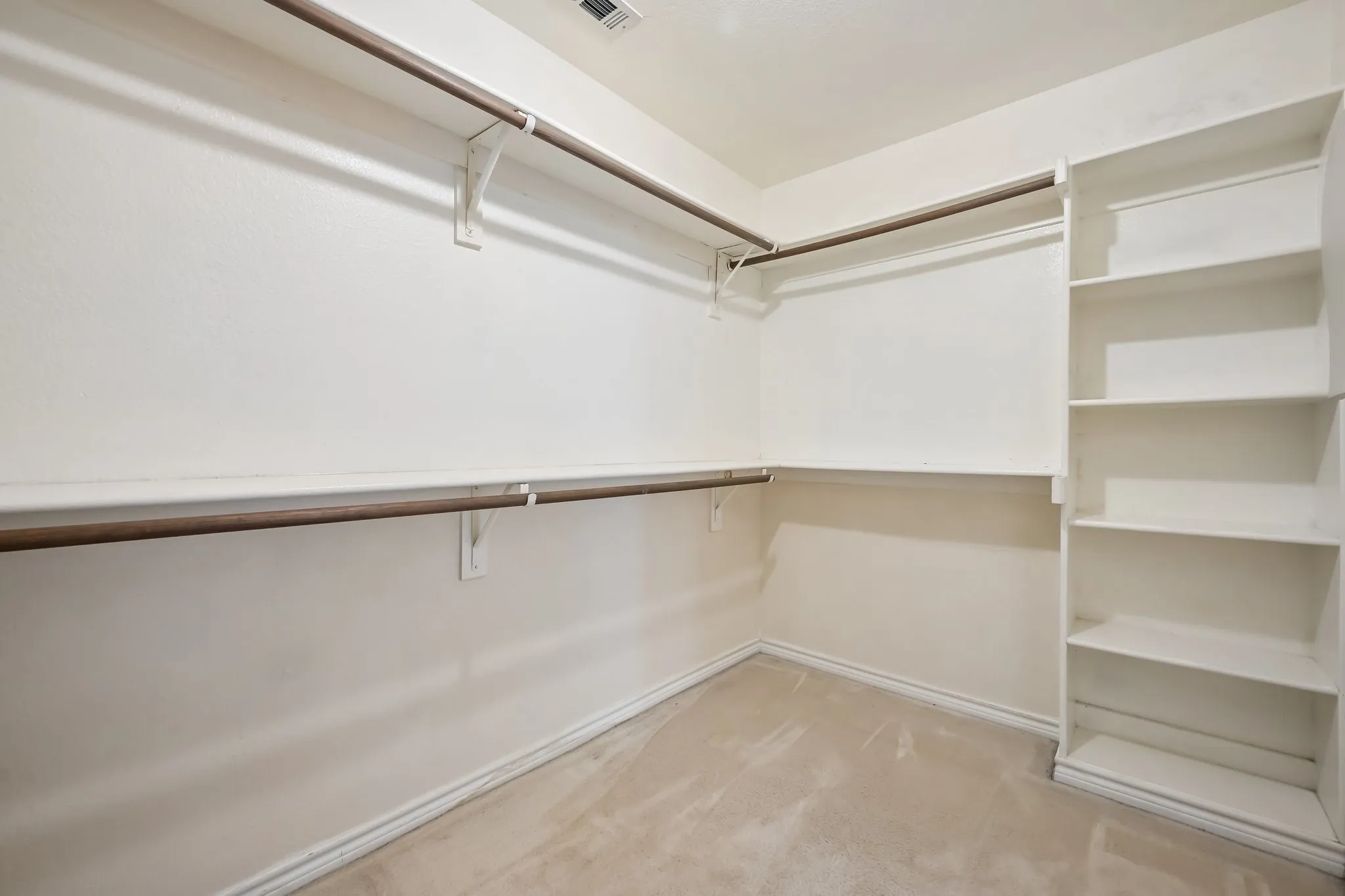 Walk-in closet with beige carpet flooring, built-in shelving, and multiple clothing rods