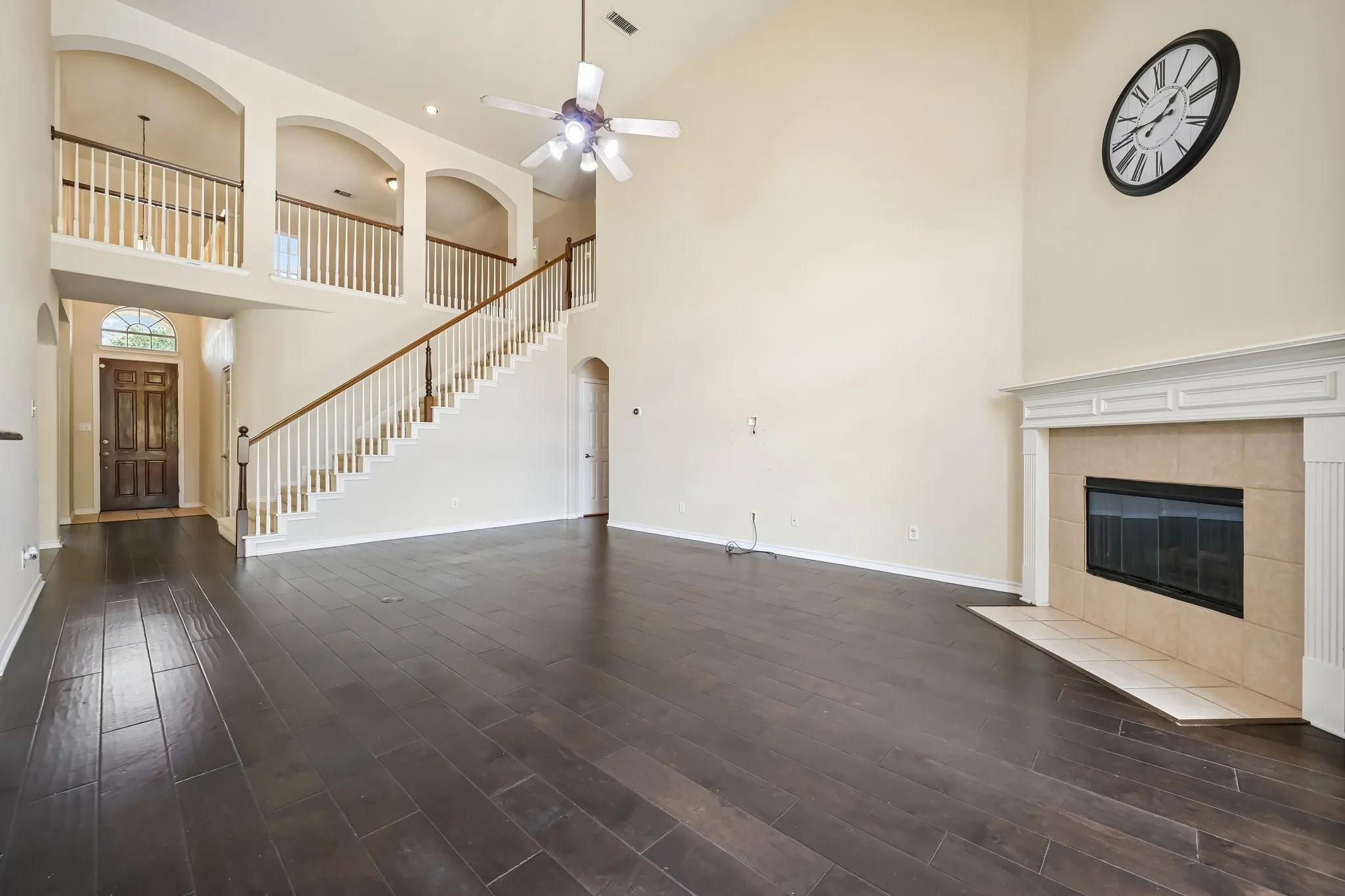 Two-story living area featuring dark wood-finish flooring, a fireplace with a light-colored tile surround and white mantel, and a grand staircase with white balusters and wood handrails