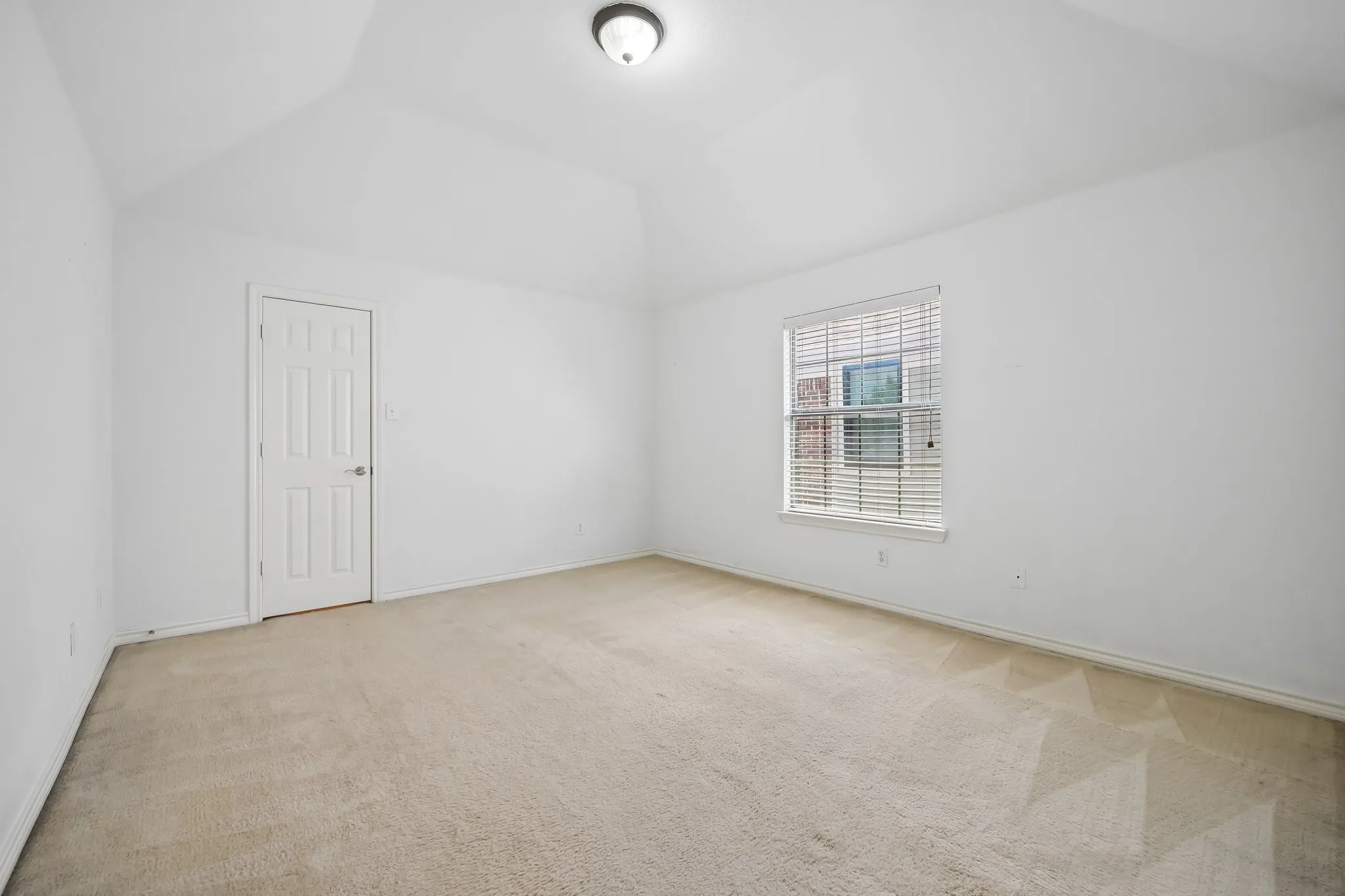 Vaulted ceiling room with neutral carpet flooring, a single window with blinds, and a six-panel door
