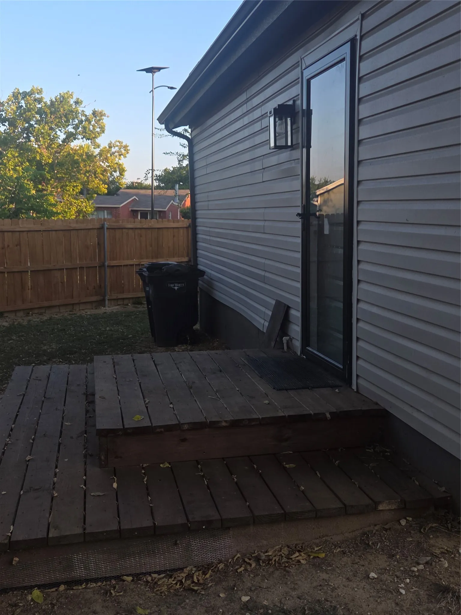 Exterior siding in a neutral tone features a black-framed glass door with an exterior lantern light fixture