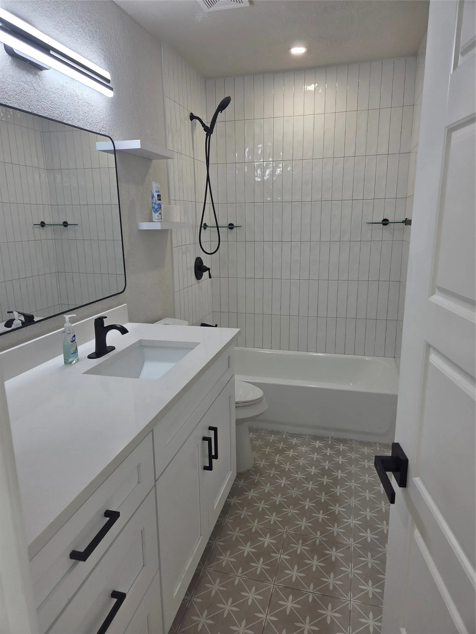 Bathroom featuring a white vanity with integrated sink, matte black fixtures, patterned floor tile, white subway tile shower surround, and a white bathtub