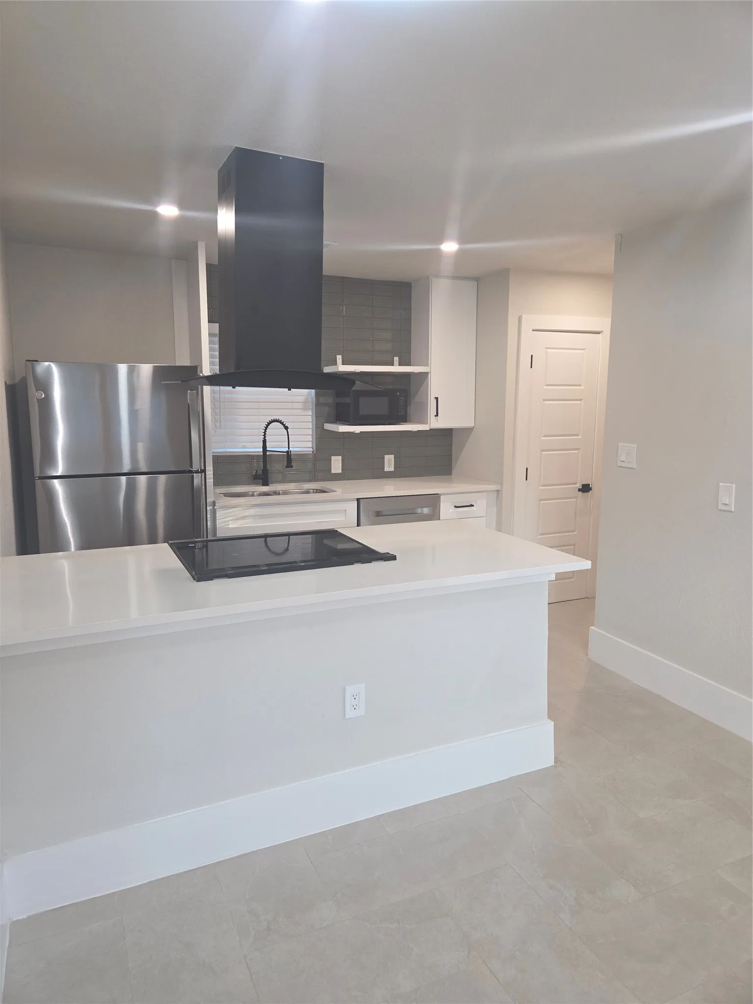 Modern kitchen featuring a stainless steel refrigerator, white cabinetry, integrated cooktop, and a matte black range hood