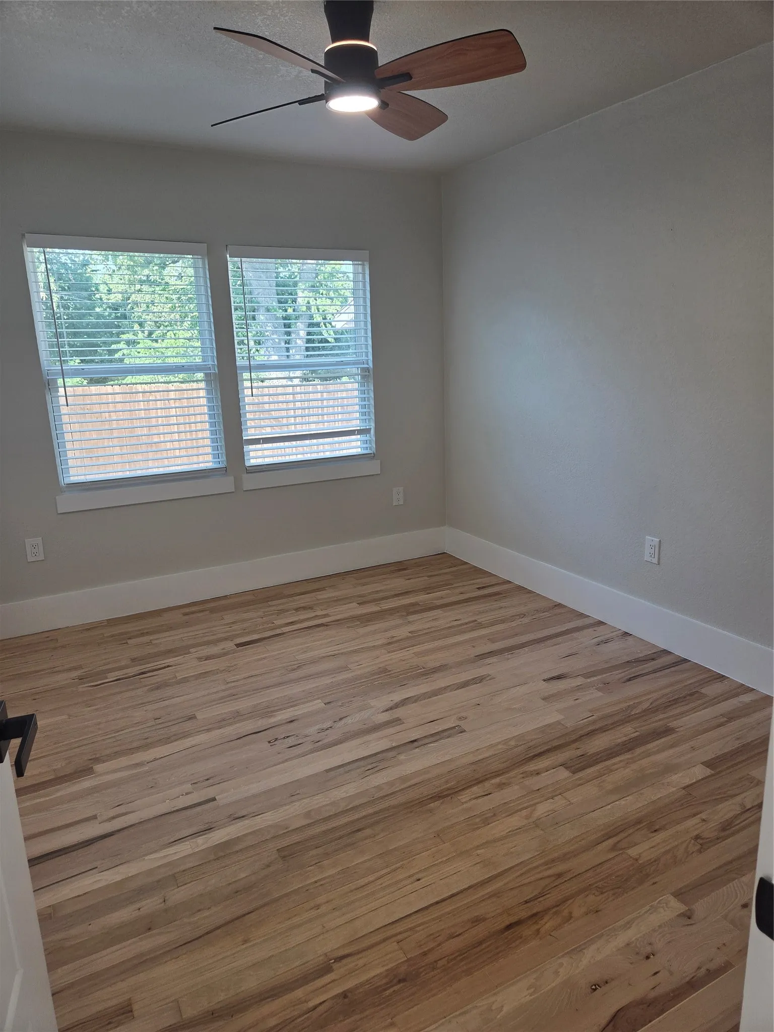 Spacious room featuring wood-finish flooring, white baseboards, and neutral wall tones