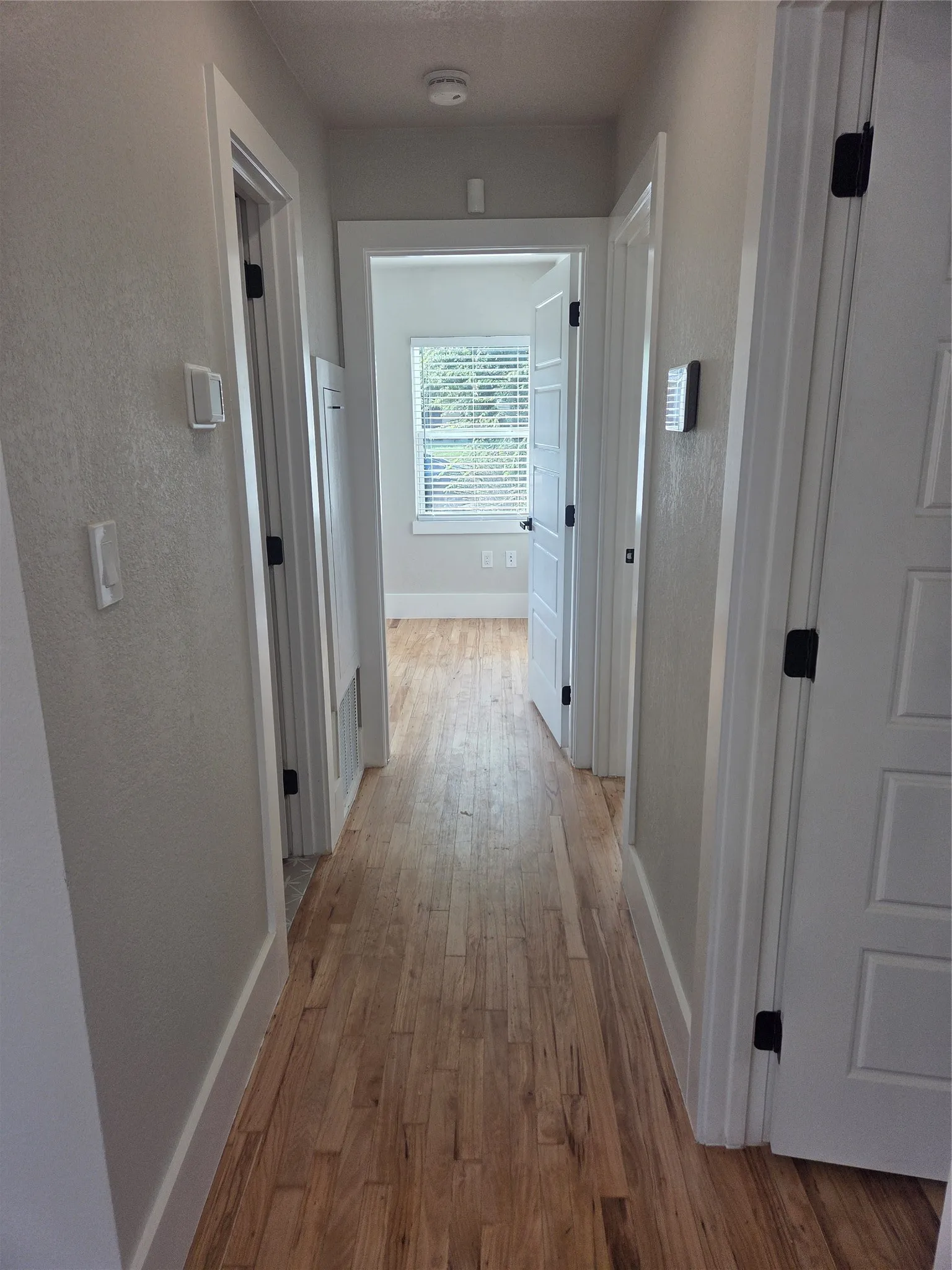 Hallway featuring wood-finish flooring, light-toned wall paint, white trim, and white paneled doors with black hardware