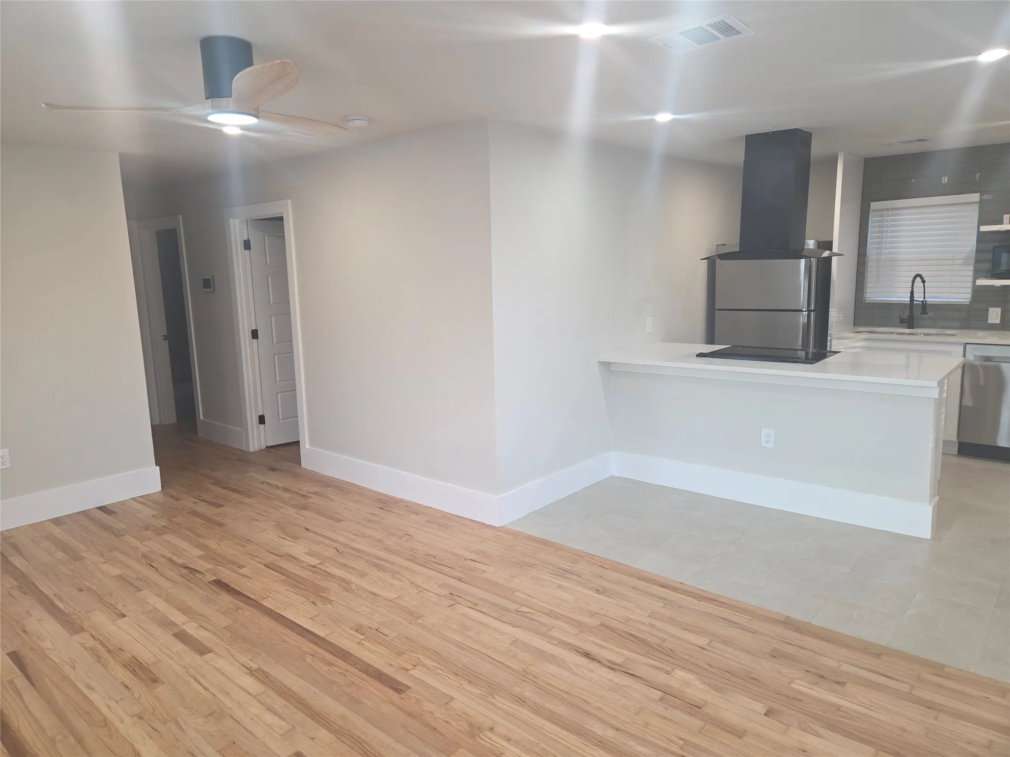 Open-concept living space featuring wood-finish flooring, a modern ceiling fan with lighting, and a kitchen peninsula with a cooktop and integrated downdraft ventilation