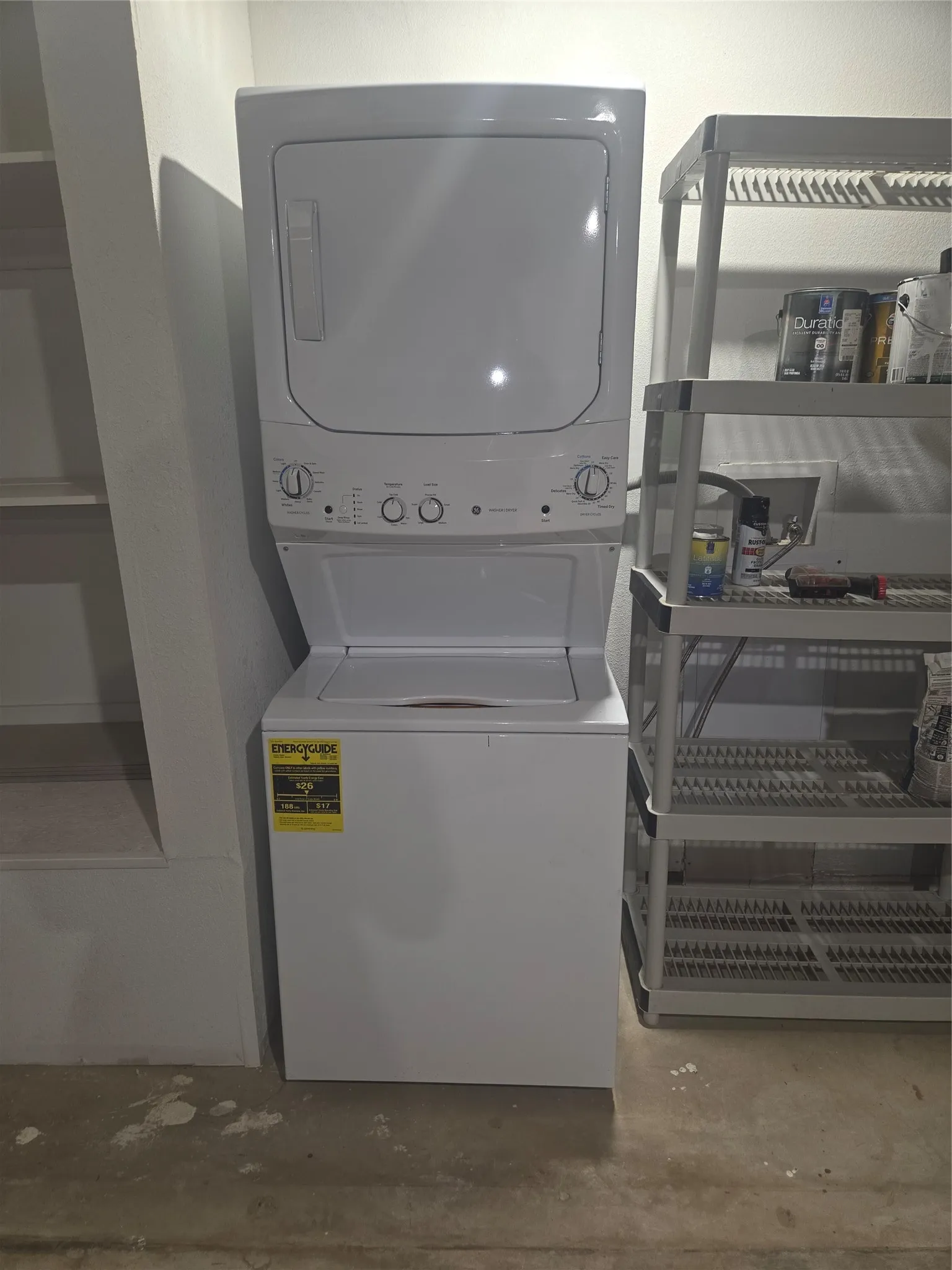 Dedicated utility area featuring a white stackable washer and dryer unit, built-in shelving, and a concrete floor