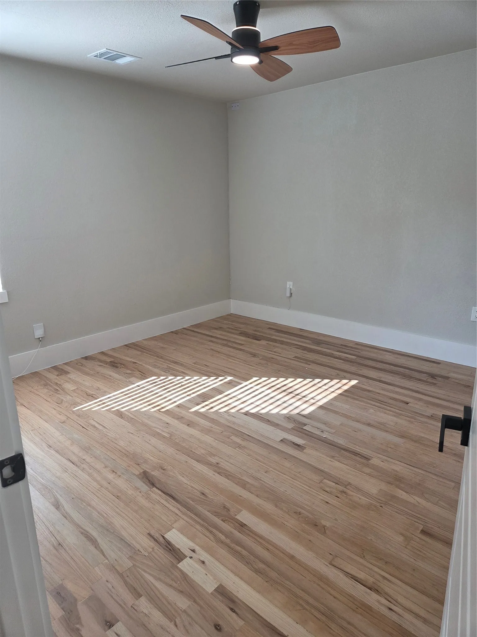 Spacious room featuring wood-finish flooring, light gray wall paint, and white baseboards