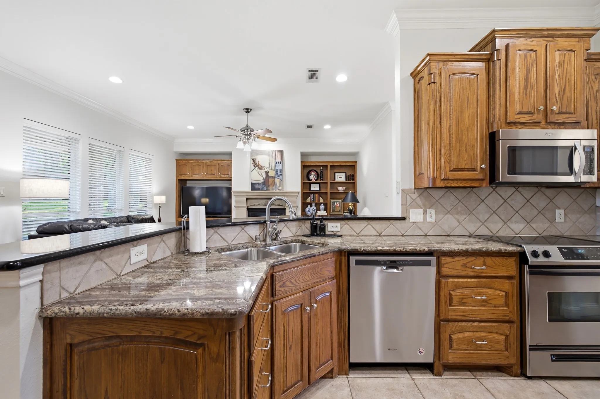 Kitchen featuring a double basin sink, stainless steel appliances, wood cabinetry, granite countertops, and tile backsplash