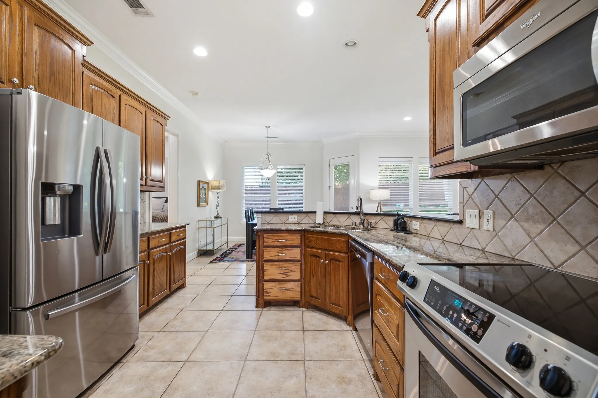 Kitchen featuring stainless steel appliances, wood cabinetry, granite countertops, and tiled flooring