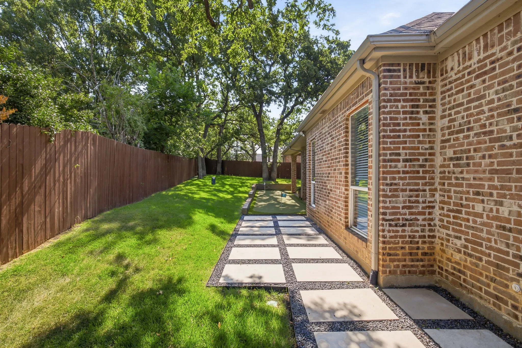 Brick exterior featuring paver pathway, manicured lawn, and privacy fencing