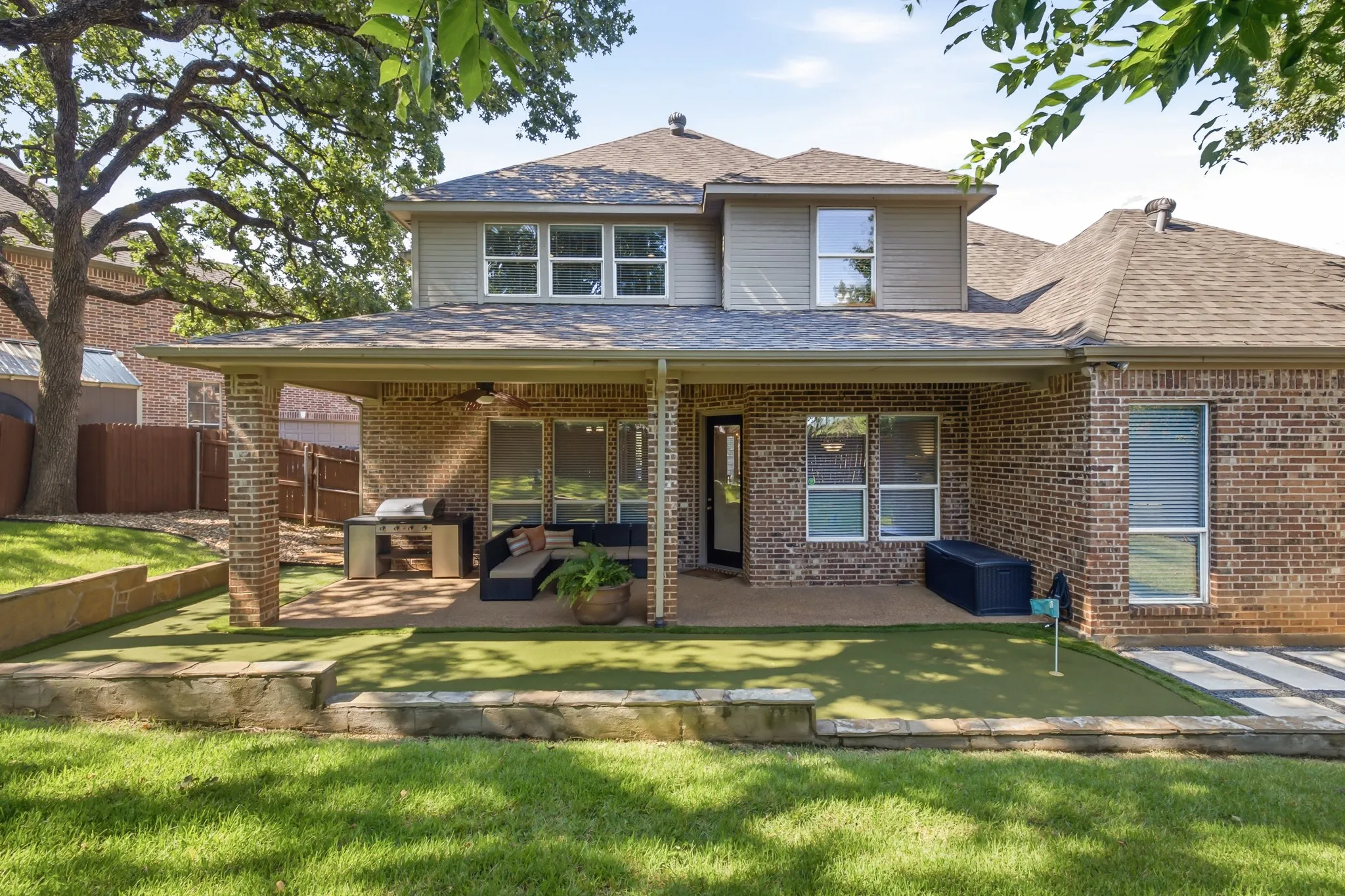 Brick exterior with a covered patio, featuring a spot for outdoor grill station and an integrated putting green