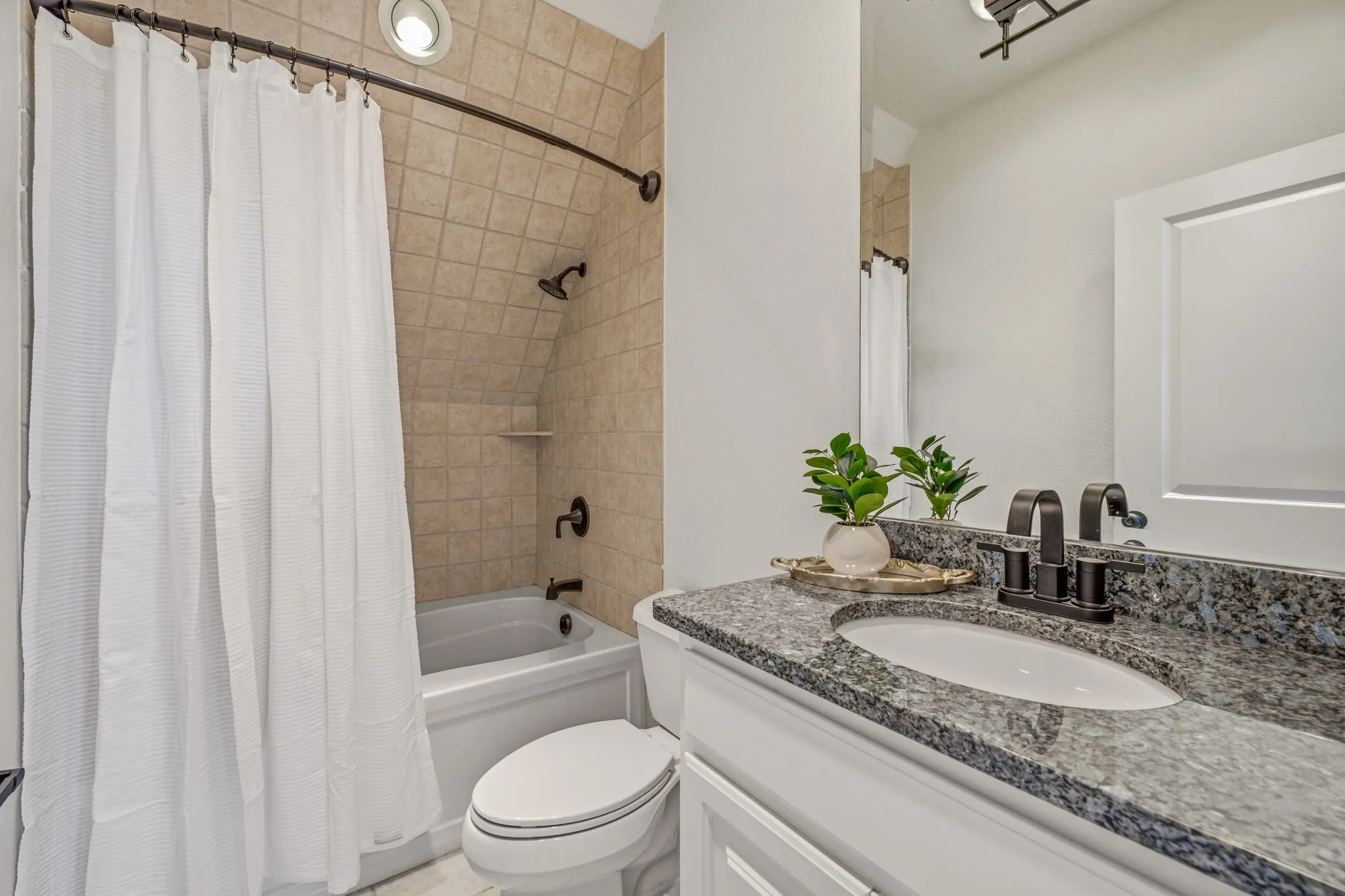 Bathroom featuring a white vanity with a granite countertop and oval undermount sink, bronze-finish faucet, full-width vanity mirror, and a tub with tiled surround