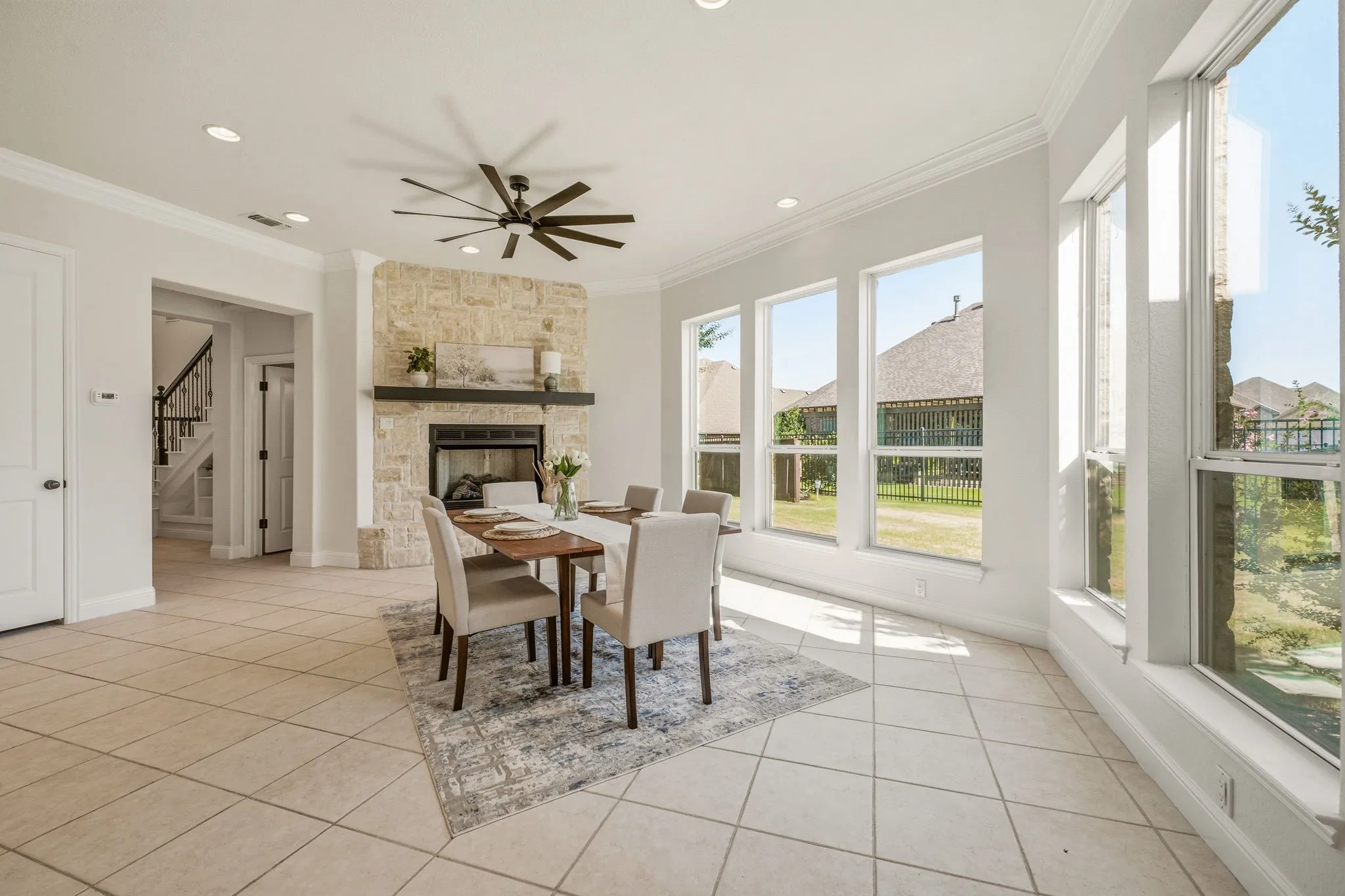 Bright dining area featuring a stone fireplace with a dark mantel, an array of tall windows, recessed lighting, and tile flooring